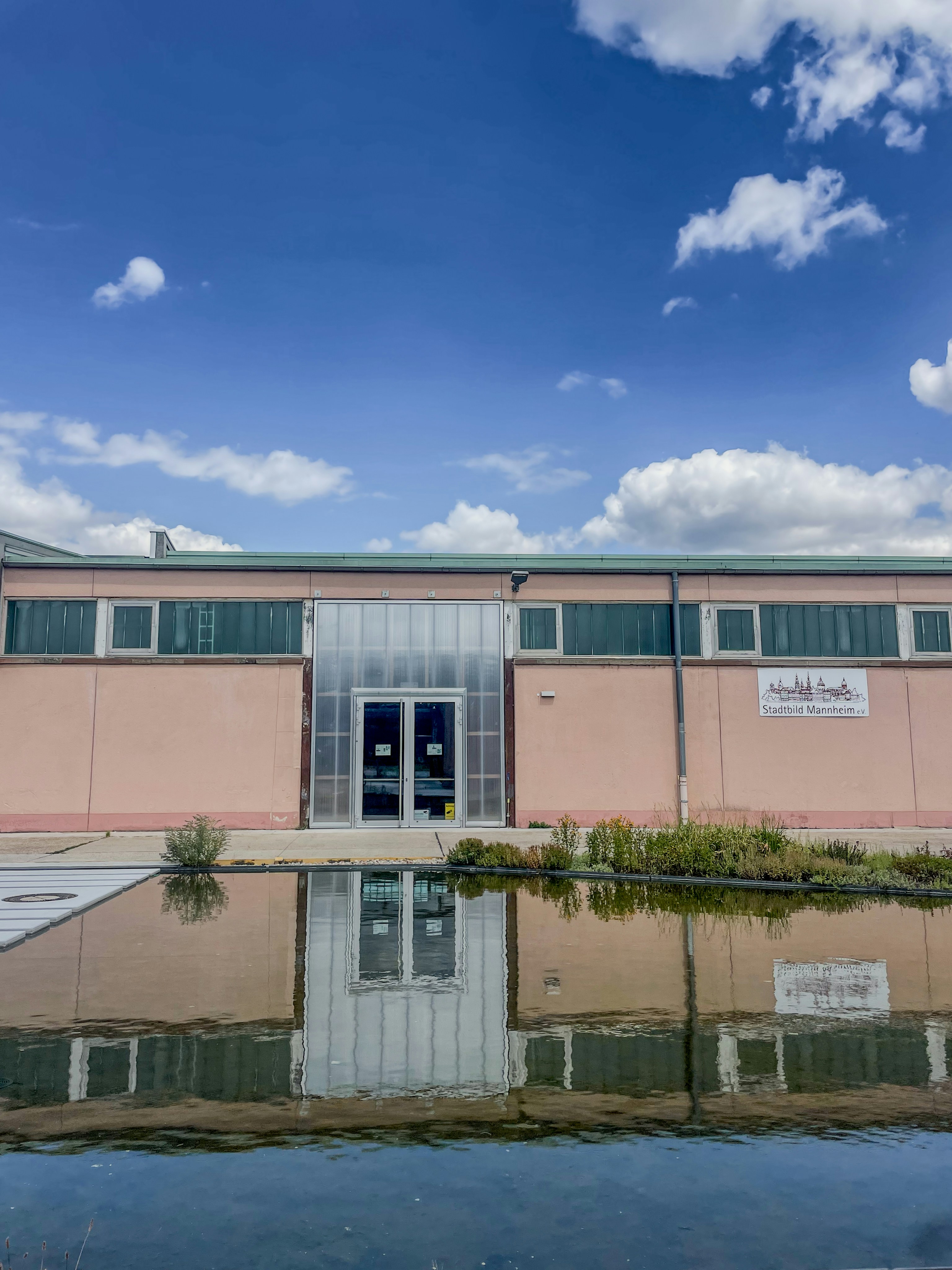 Peach building reflecting in calm water under a cloudy sky.