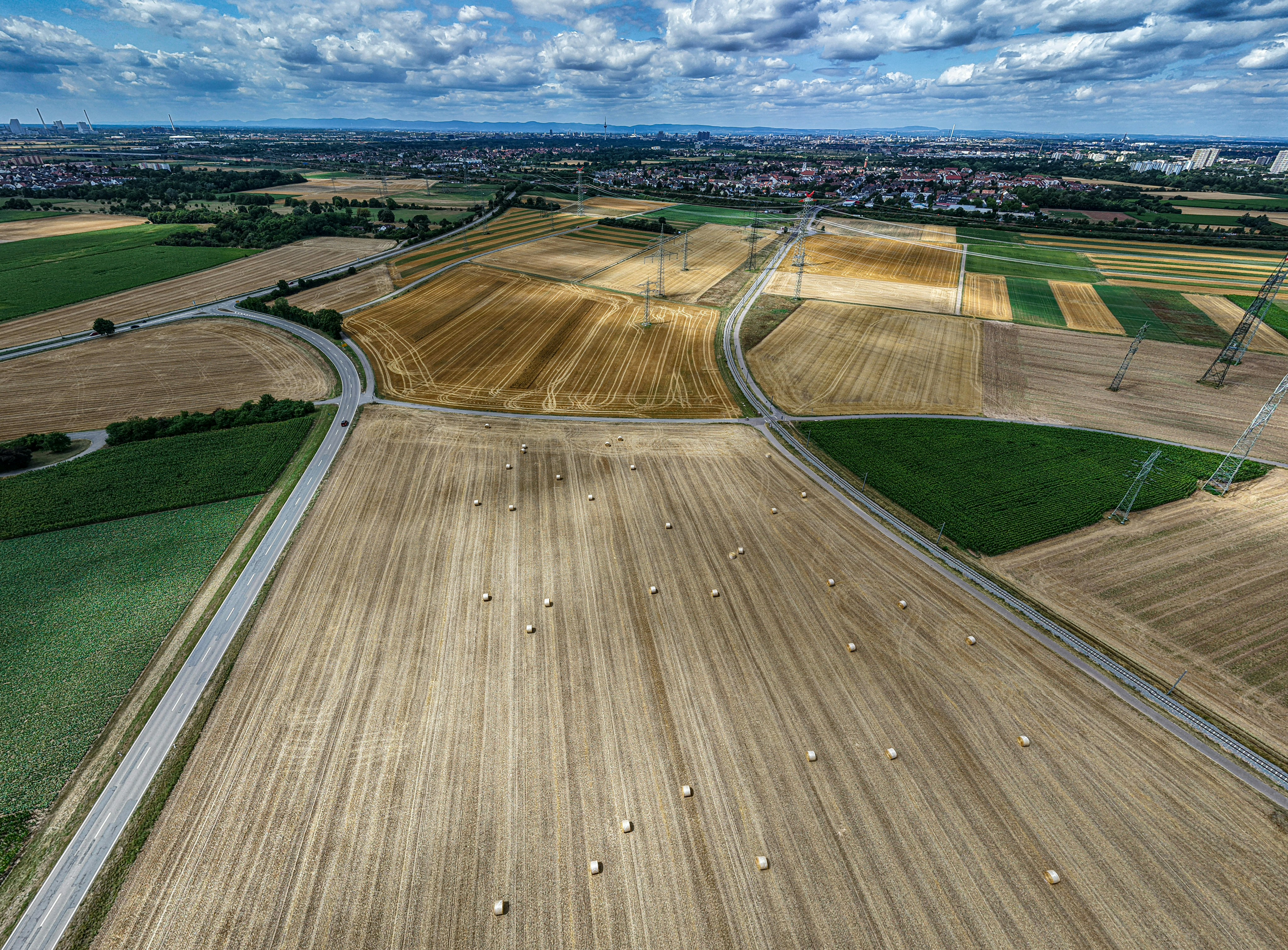 Harvested fields, winding roads, and distant town under cloudy sky.