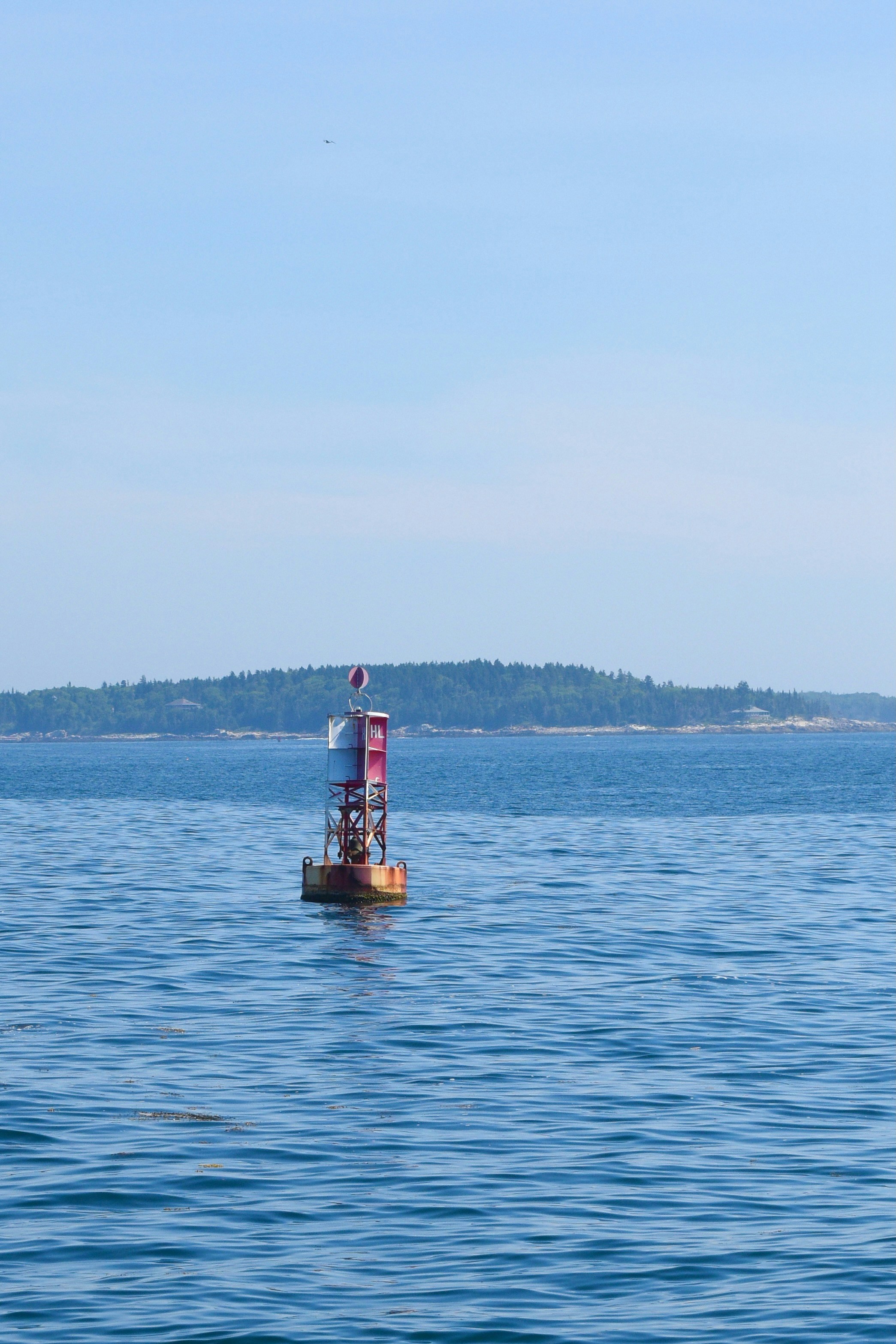 Navigation buoy floating in calm blue ocean near green island