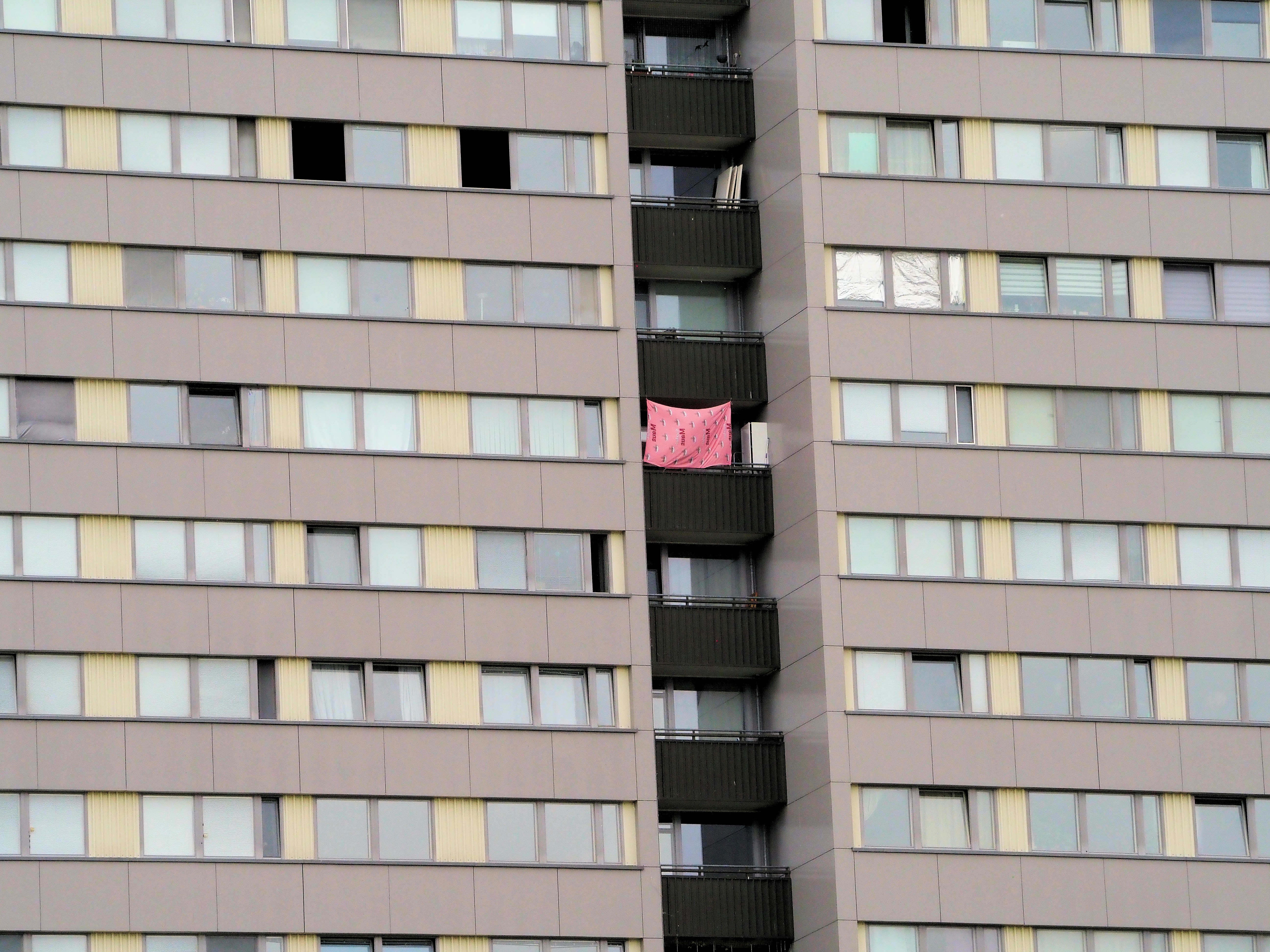 Pink towel hangs from a balcony on a grey building