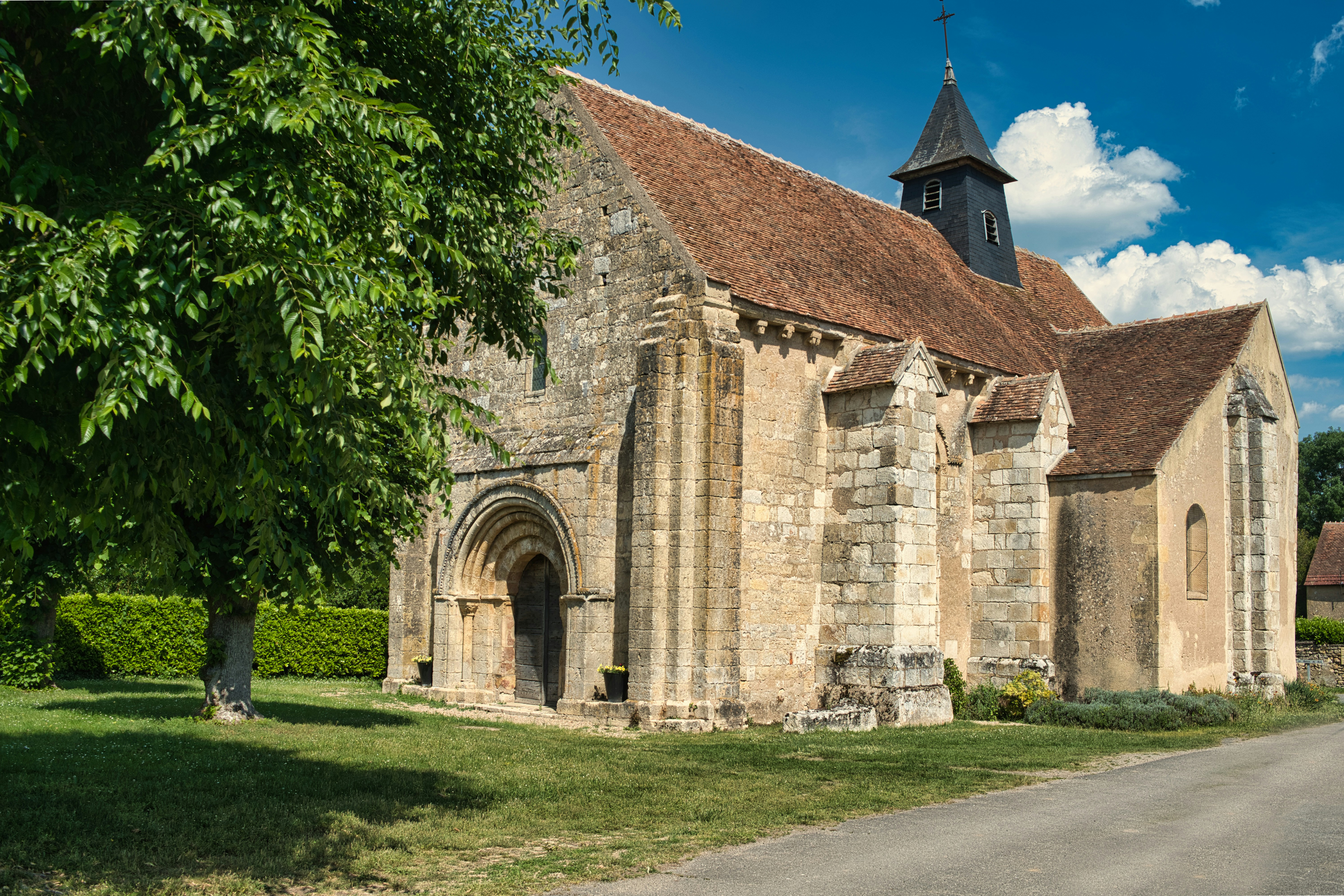 Historic stone church with a red roof and green trees.