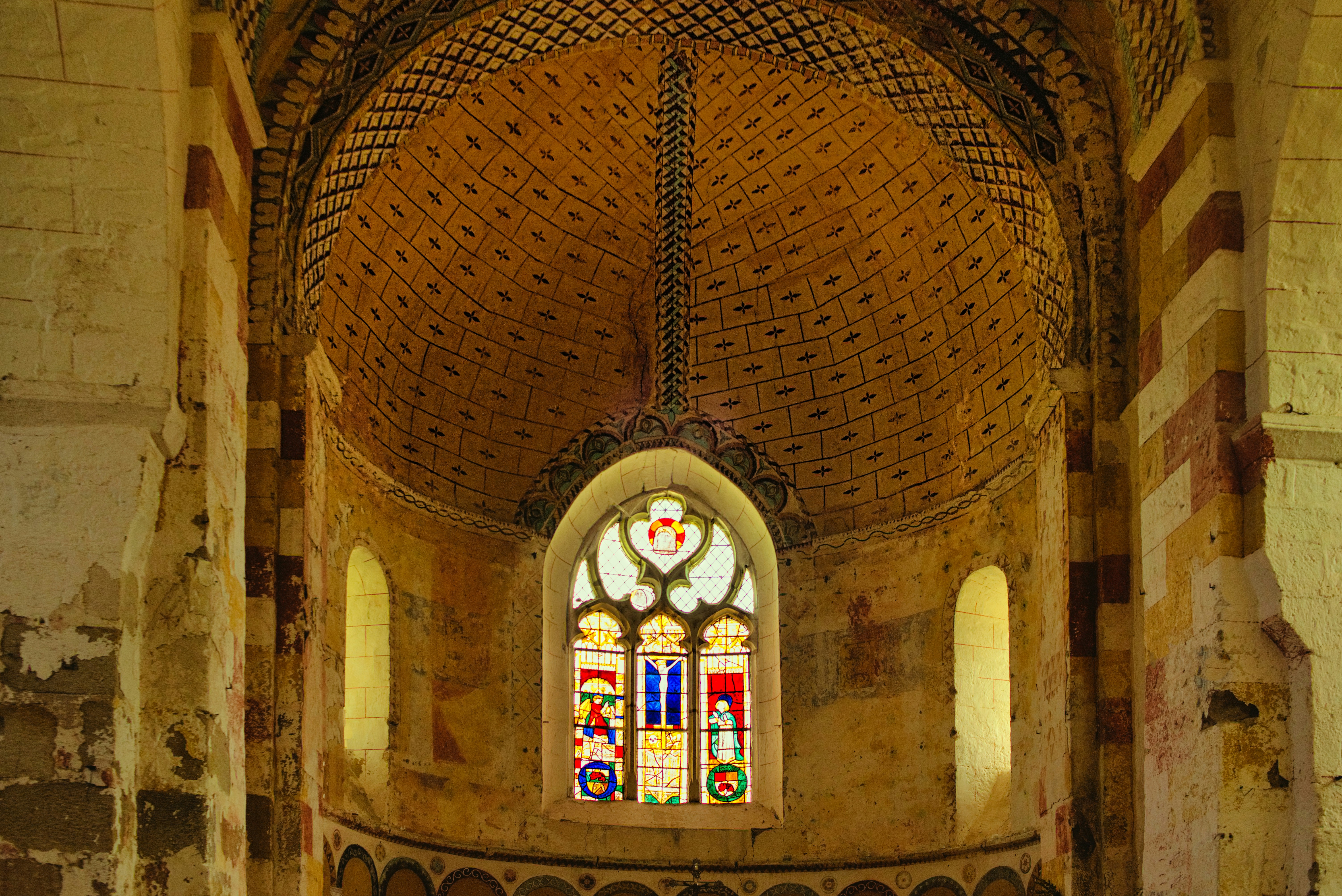 Ornate stained glass window and patterned ceiling in ancient church.