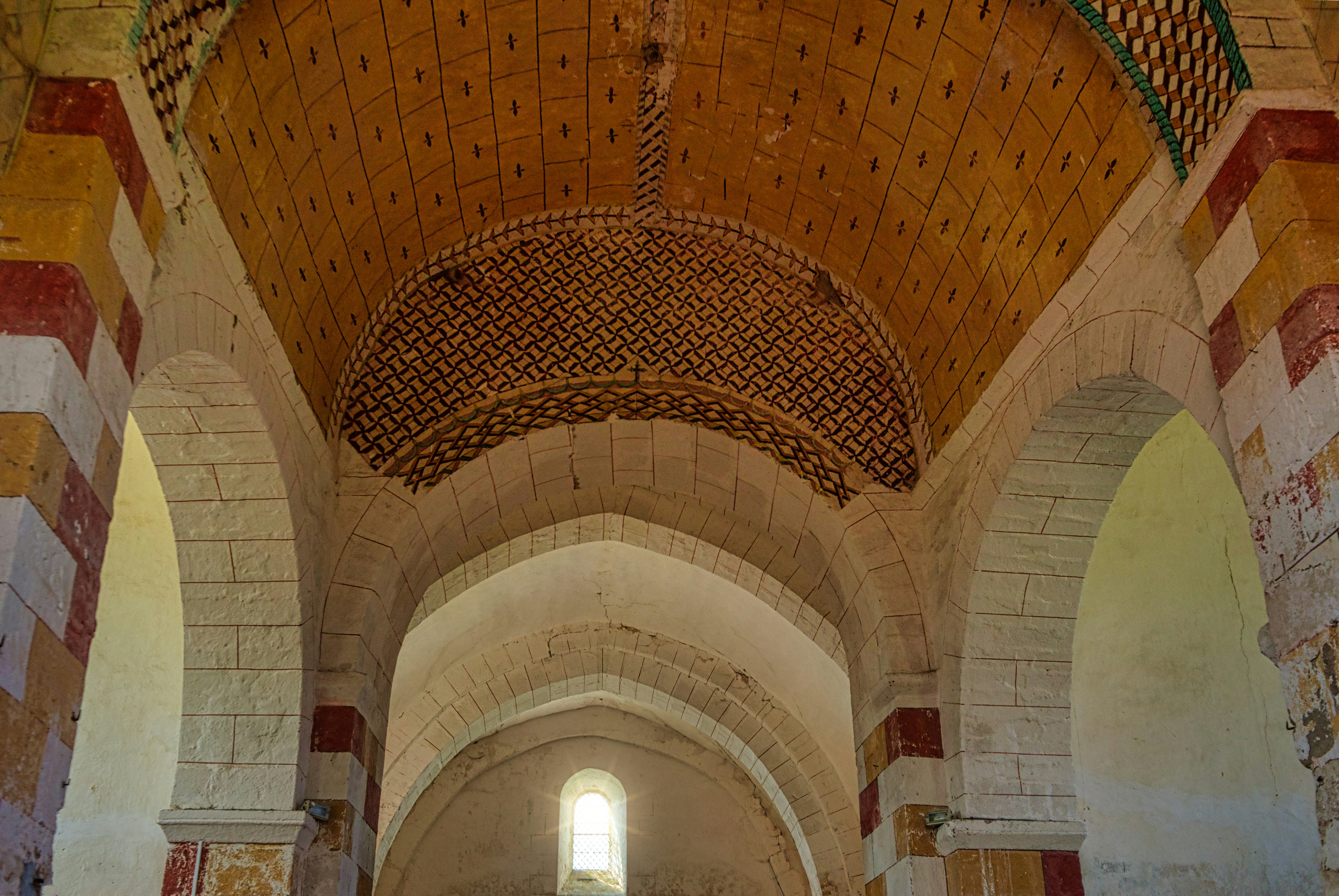 Ancient building interior with vaulted stone ceilings and painted details.