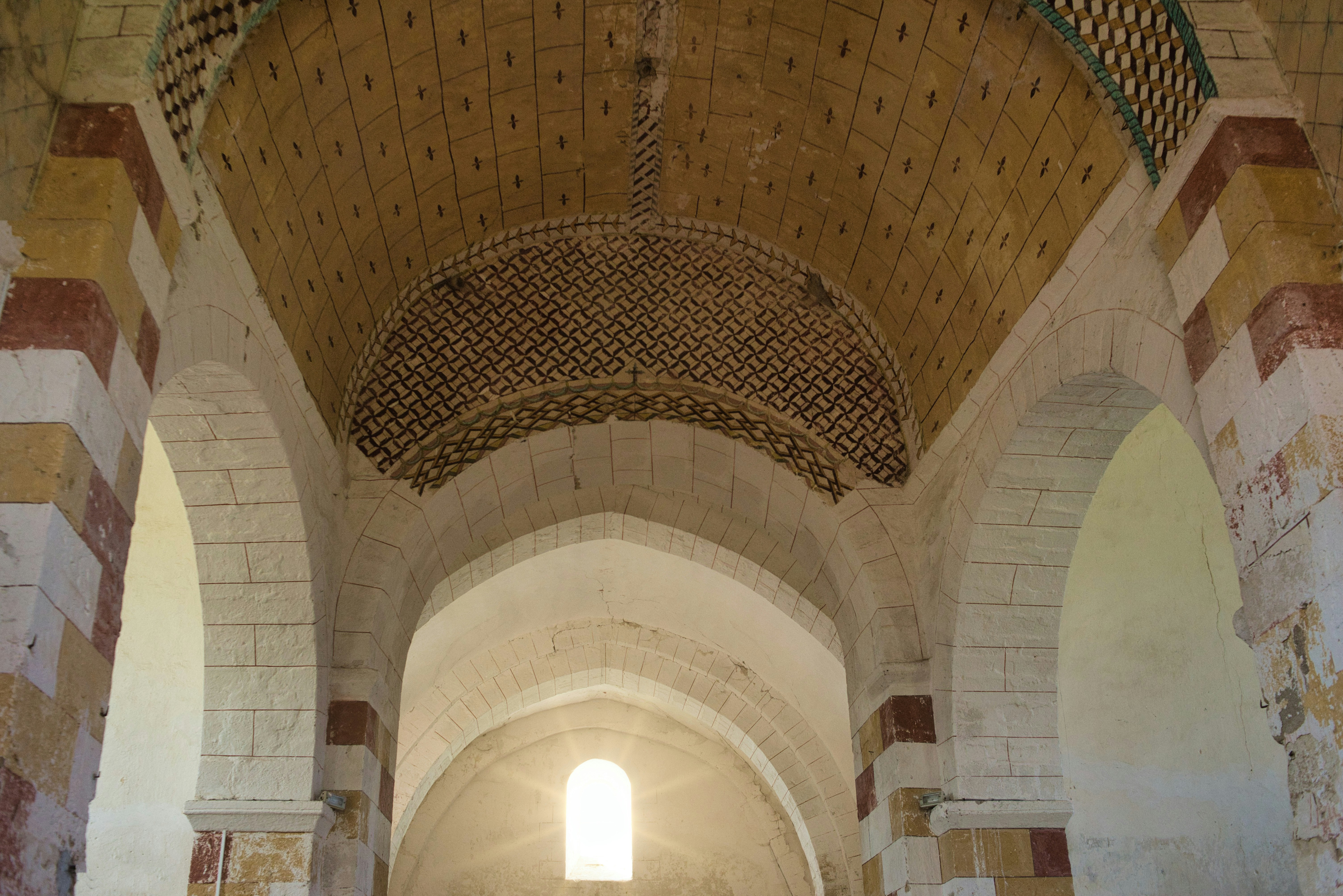 Arched stone interior with decorative ceiling and window light.