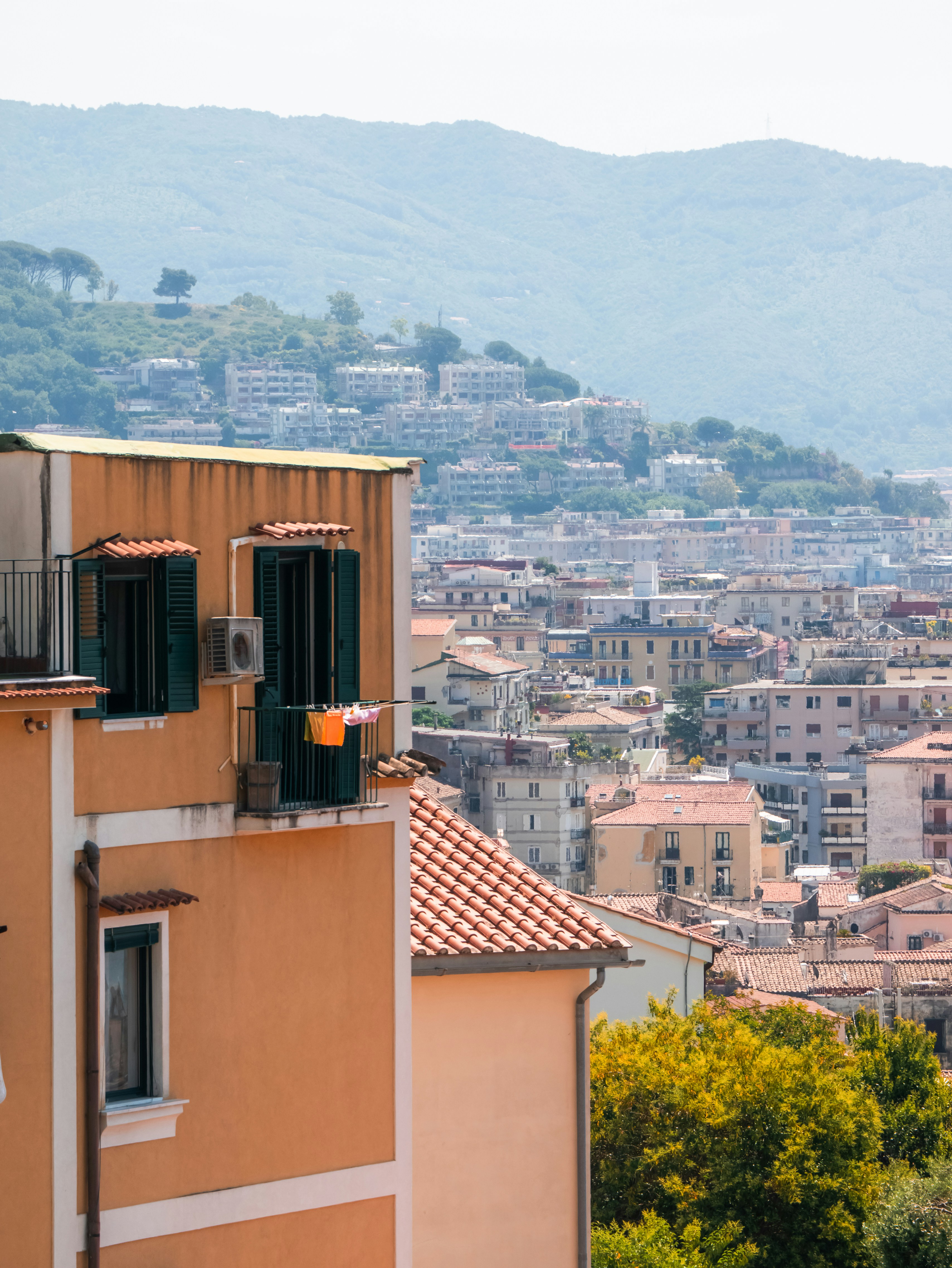 Orange building with green shutters overlooking a city and mountains