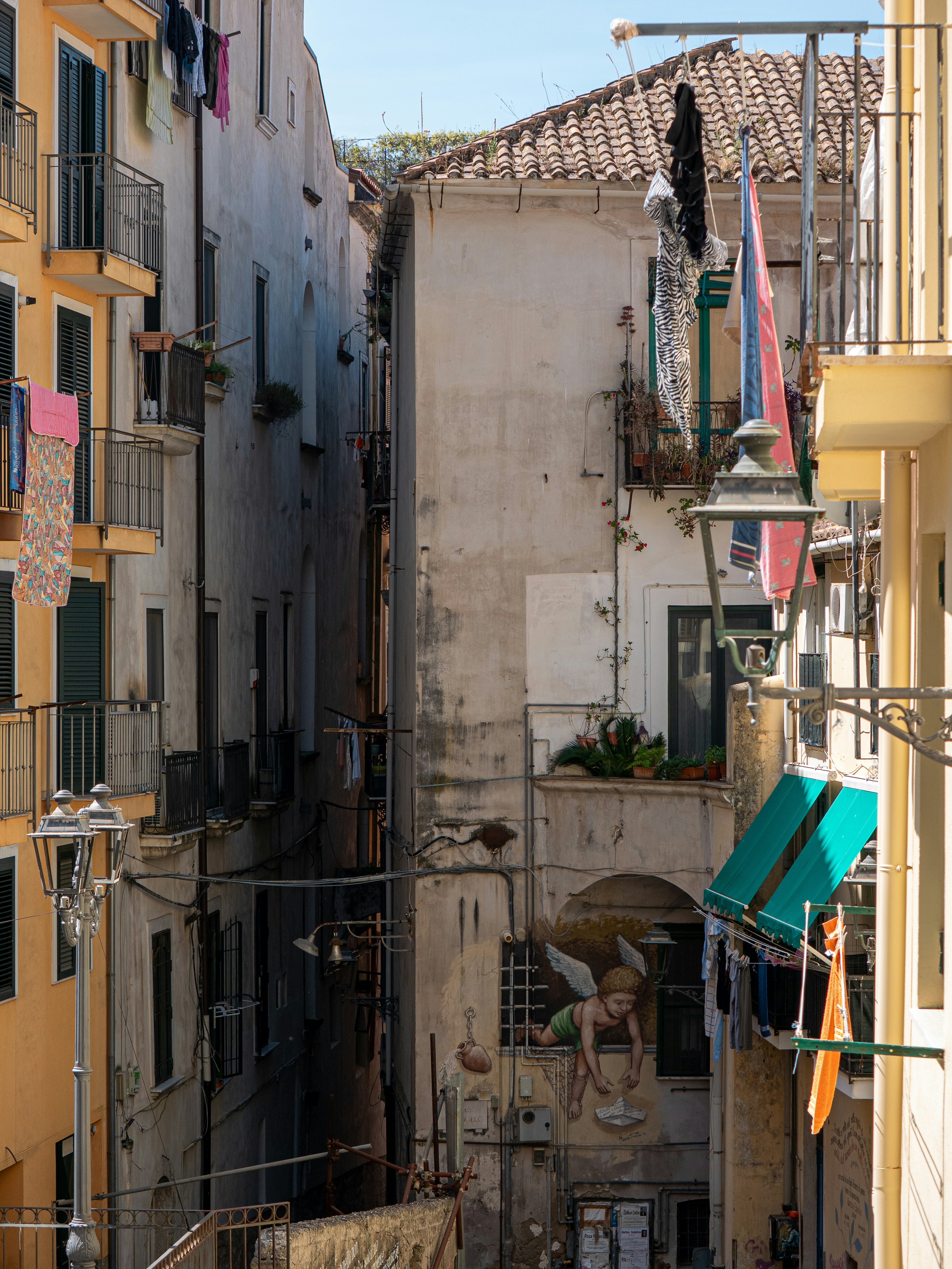 Narrow alley with old buildings, clotheslines, and an angel mural