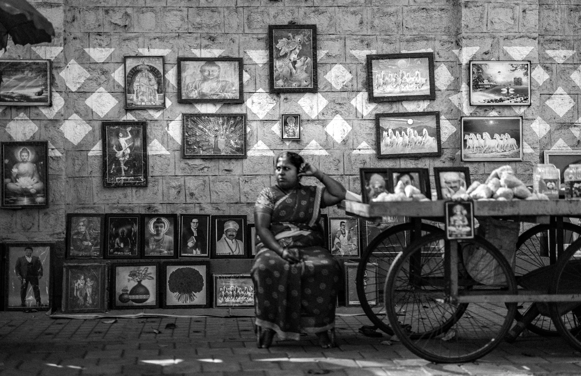 A woman sits among many framed pictures and a cart