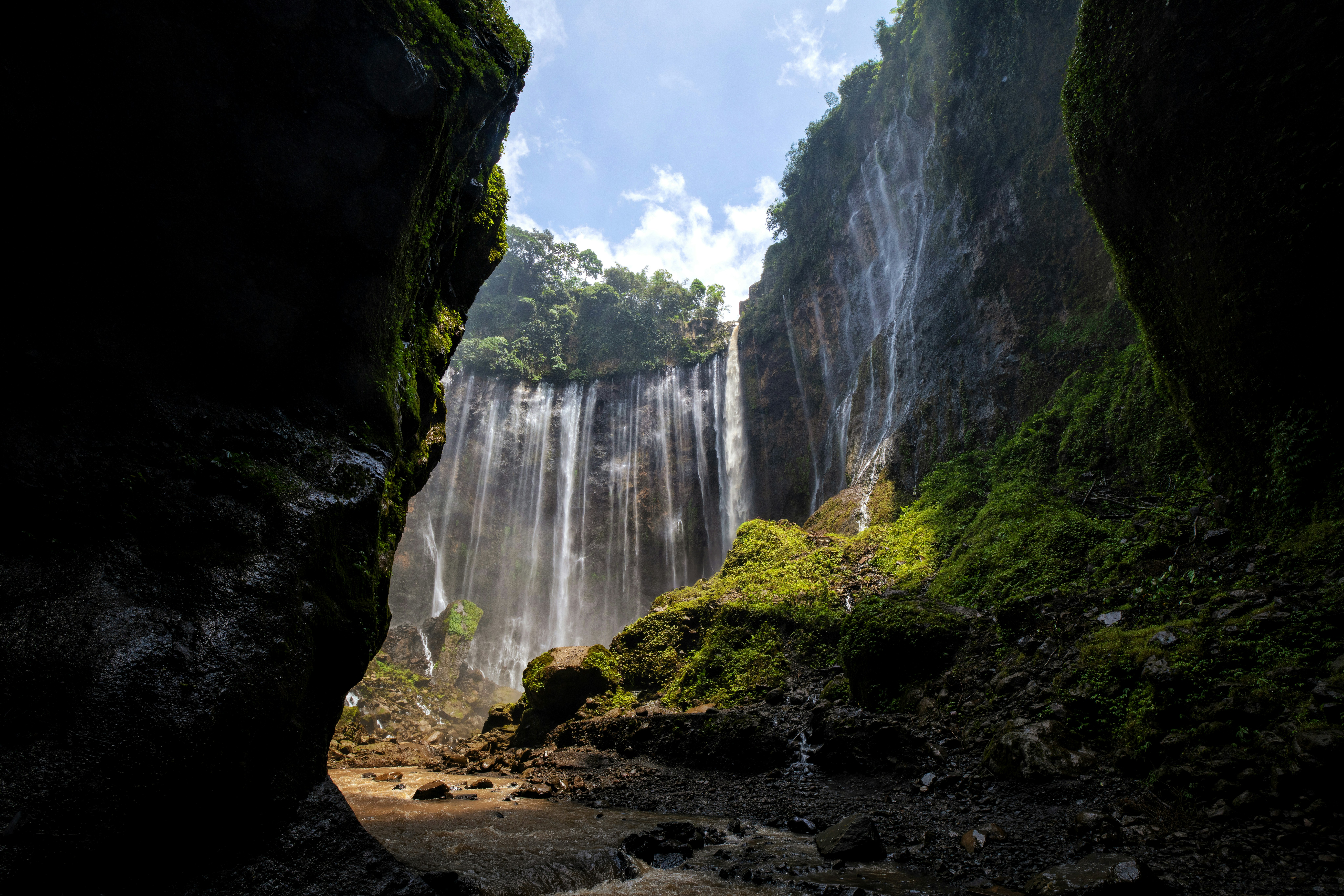 A majestic waterfall between dark cliffs under a bright sky.