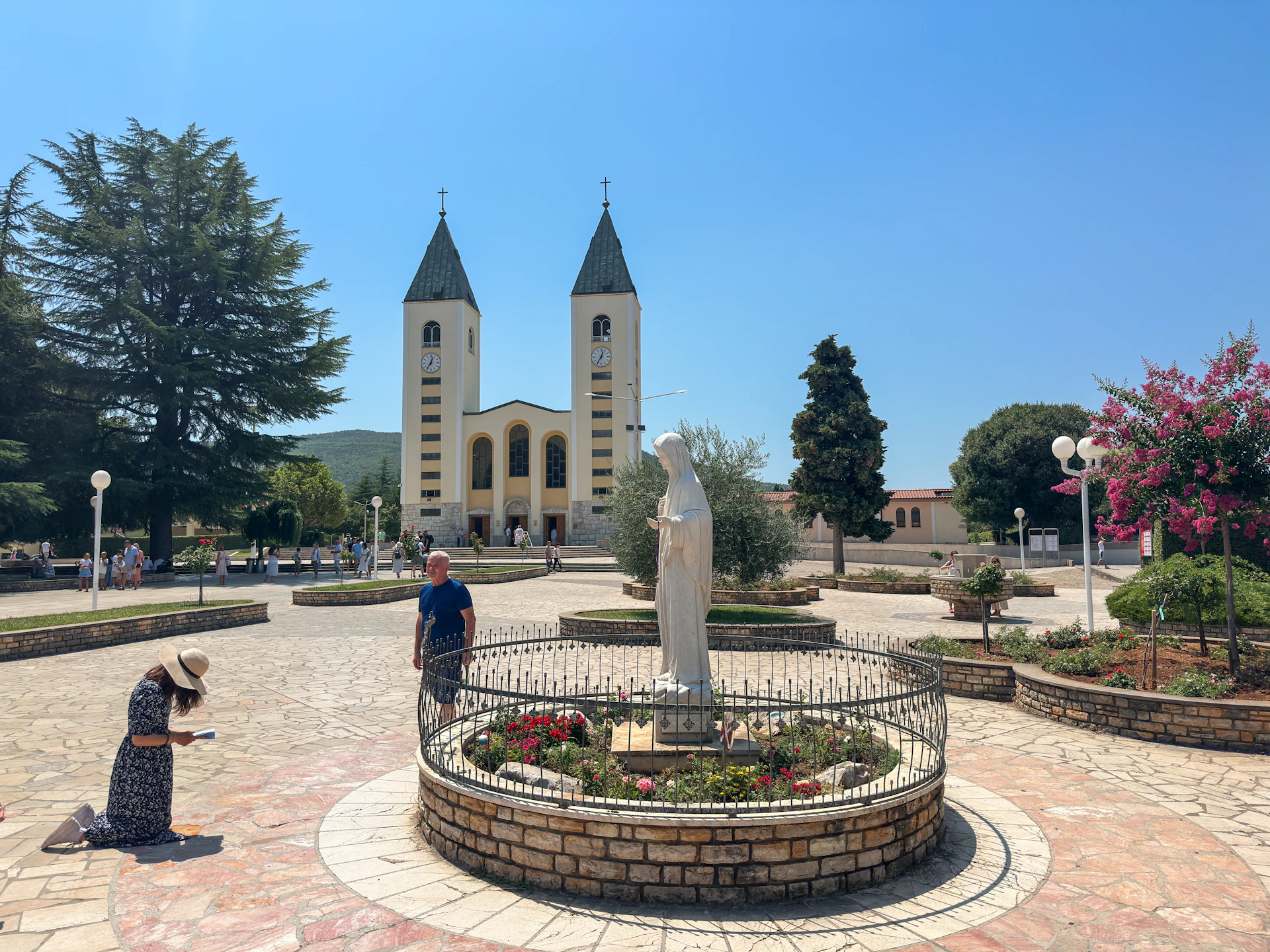 A person kneels before a statue in a church courtyard.
