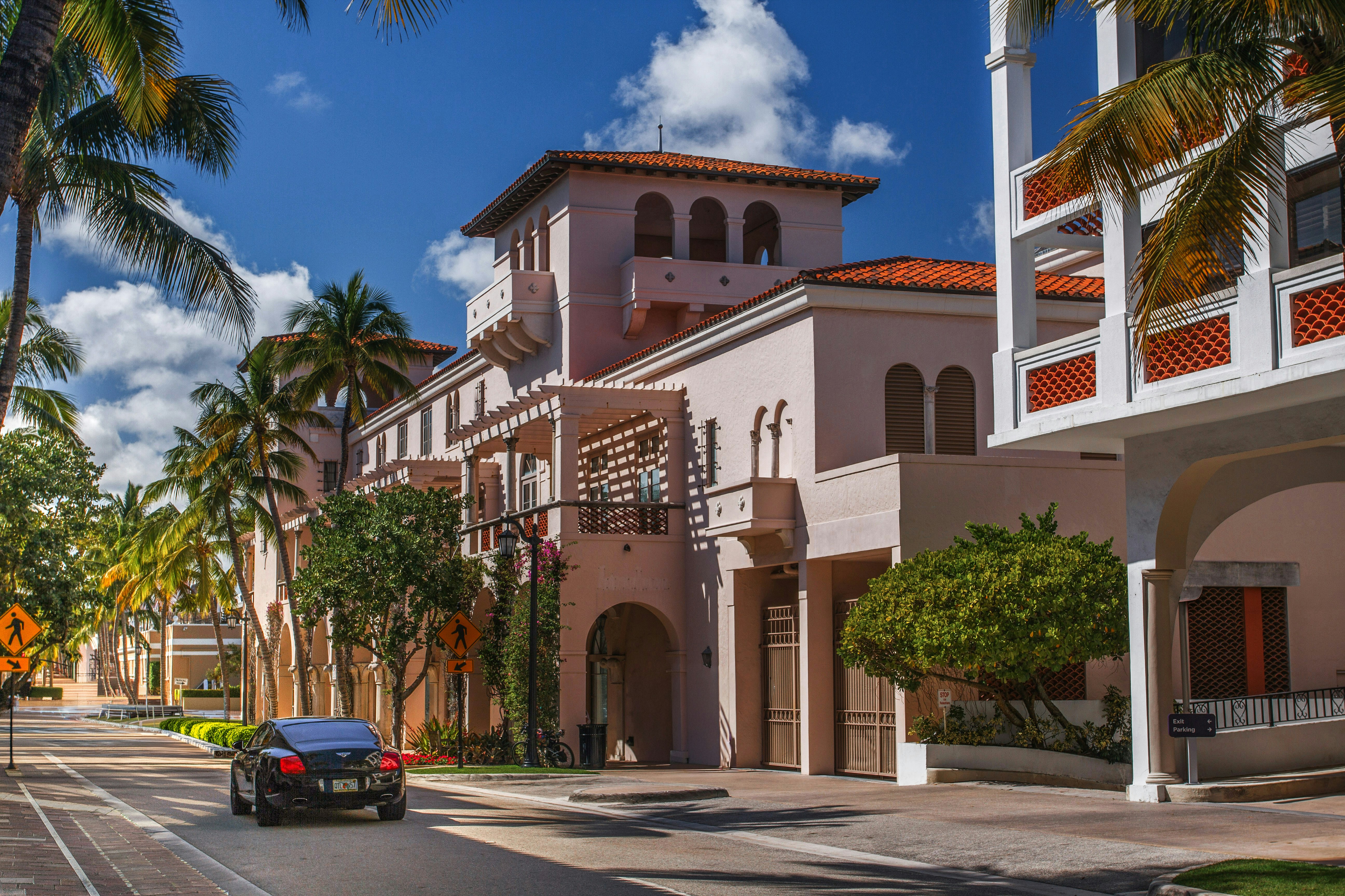 Car on street past mediterranean buildings and palm trees.