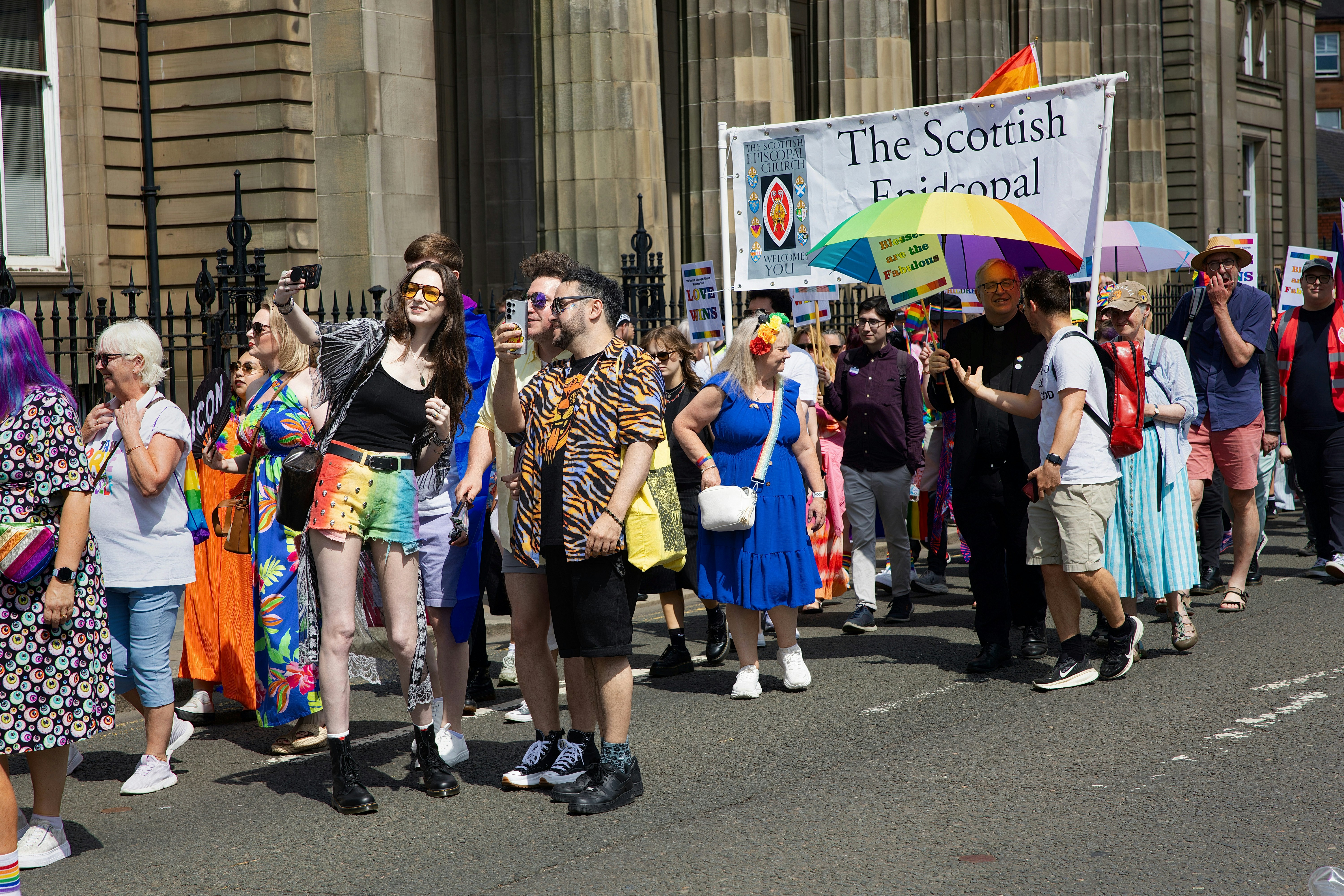 Diverse crowd marches in a vibrant street parade under sunlight.