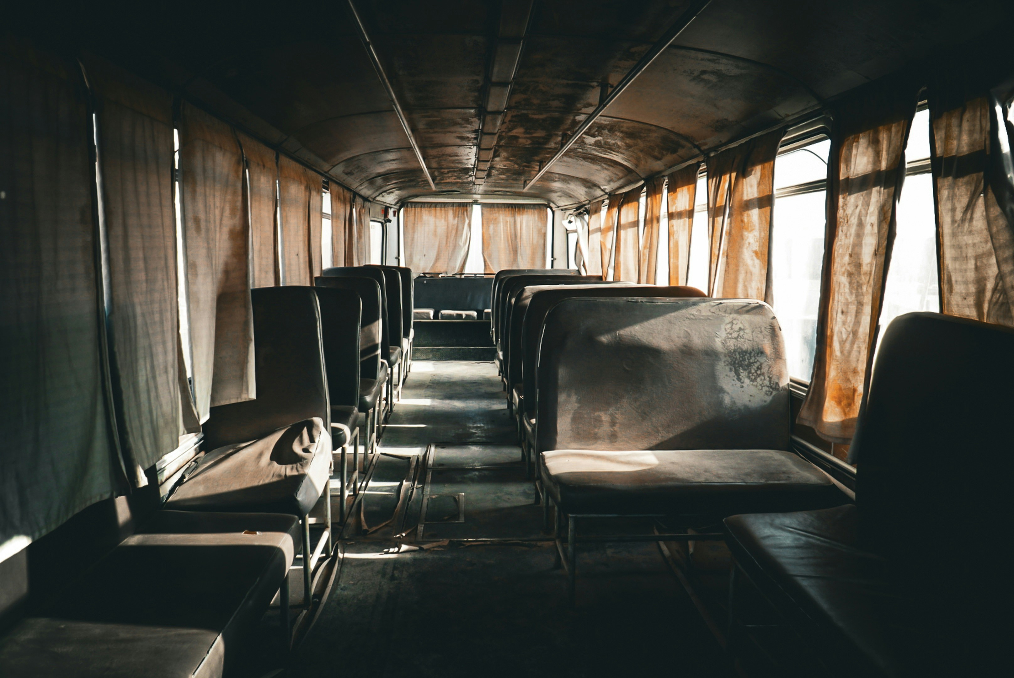 Dark, abandoned bus interior with dusty seats and worn curtains