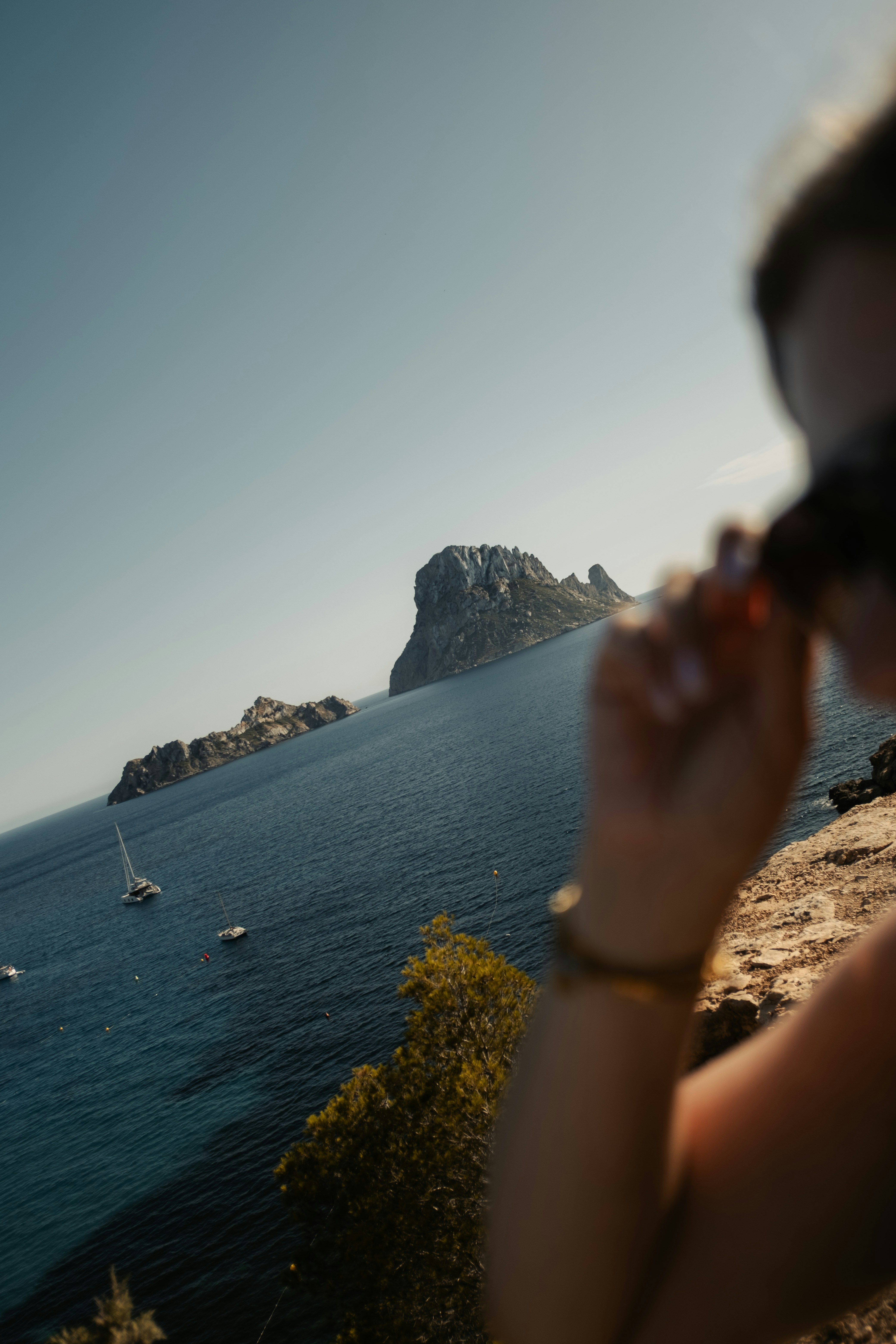 Person observes distant island and boats on the blue sea.