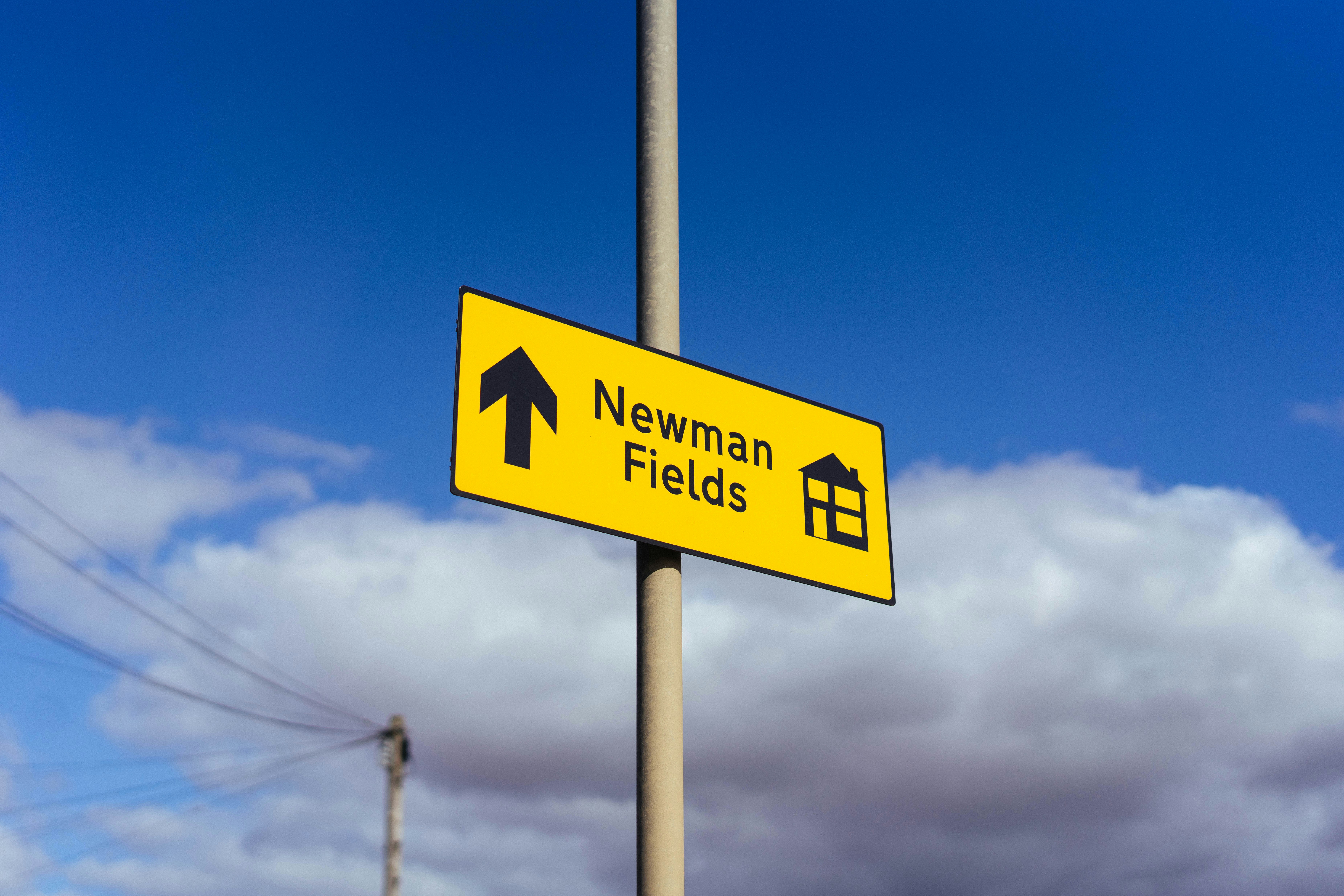 Yellow sign pointing to newman fields under blue sky.
