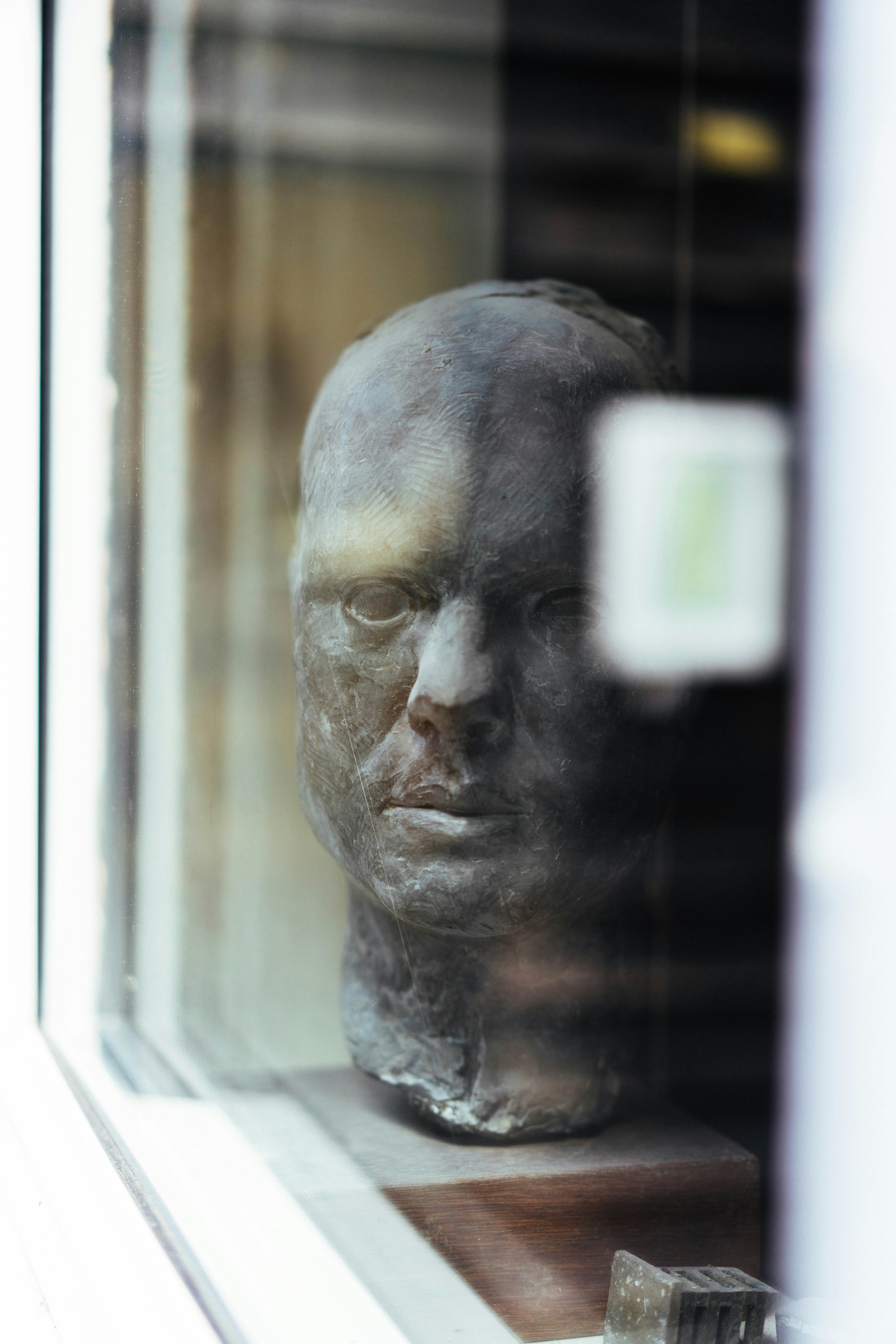 Dark sculptural head displayed behind a reflective window.