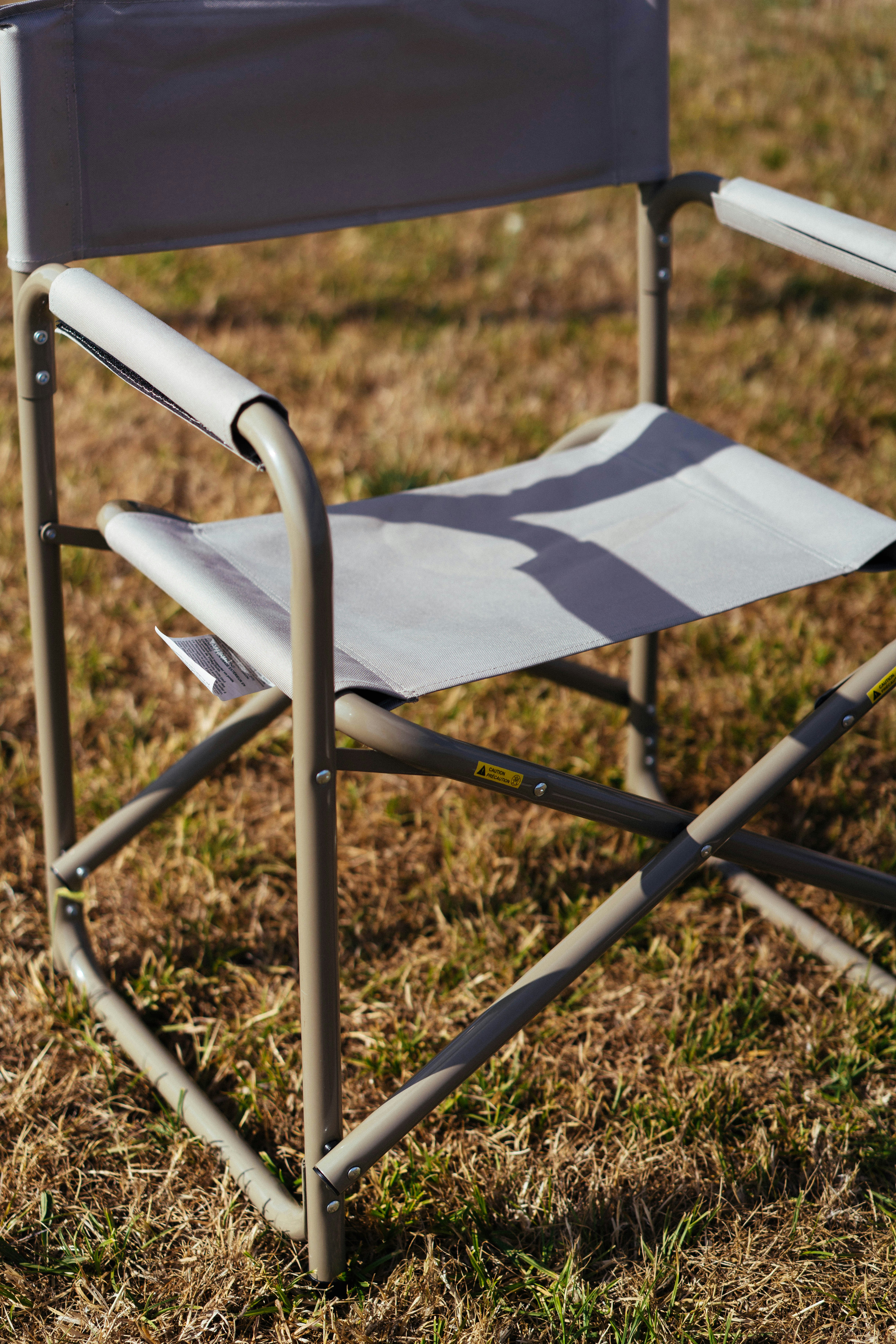 A light gray folding chair sits on dry grass outdoors.