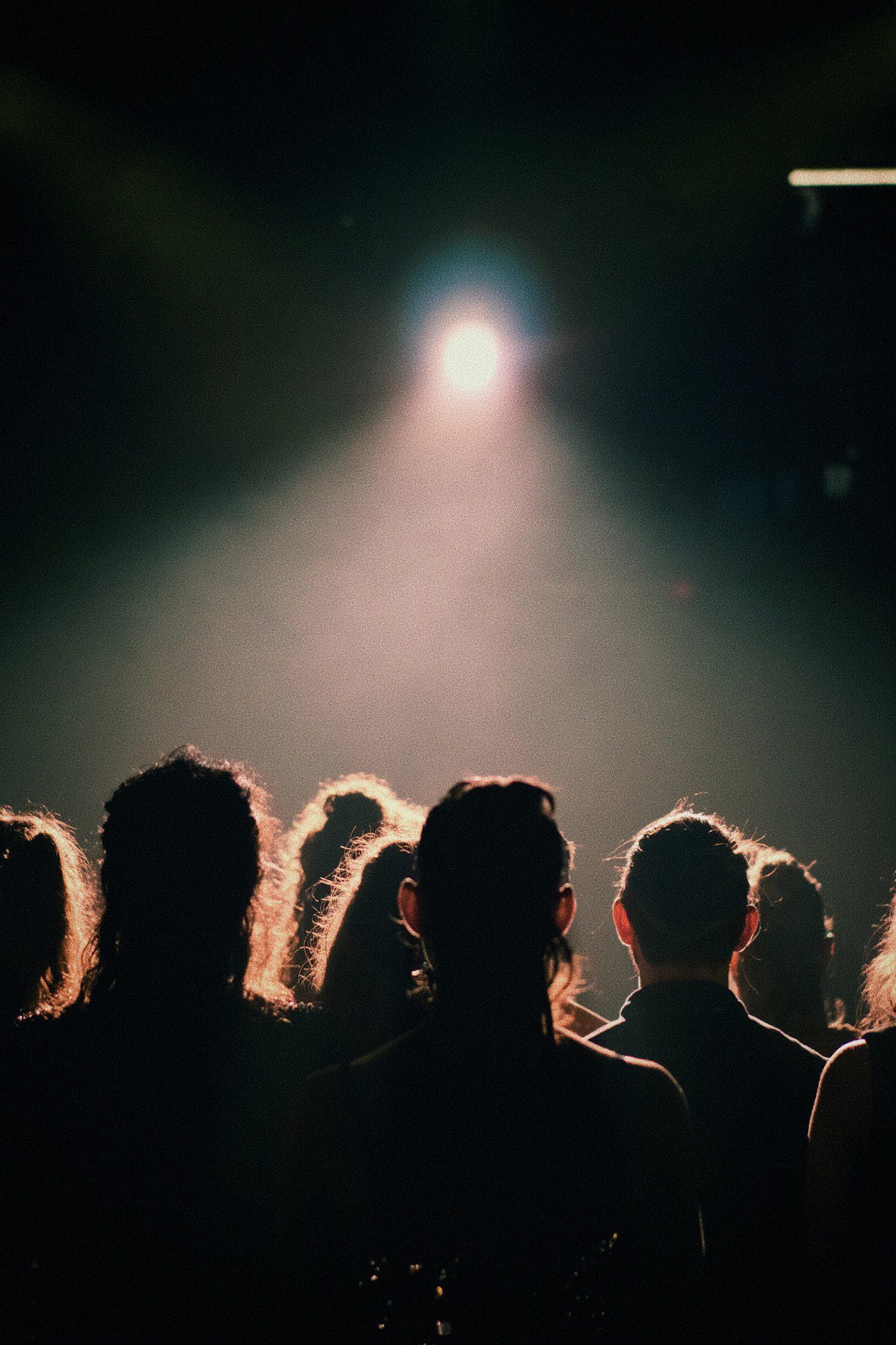 A single spotlight burning through haze above a dark, silhouetted audience