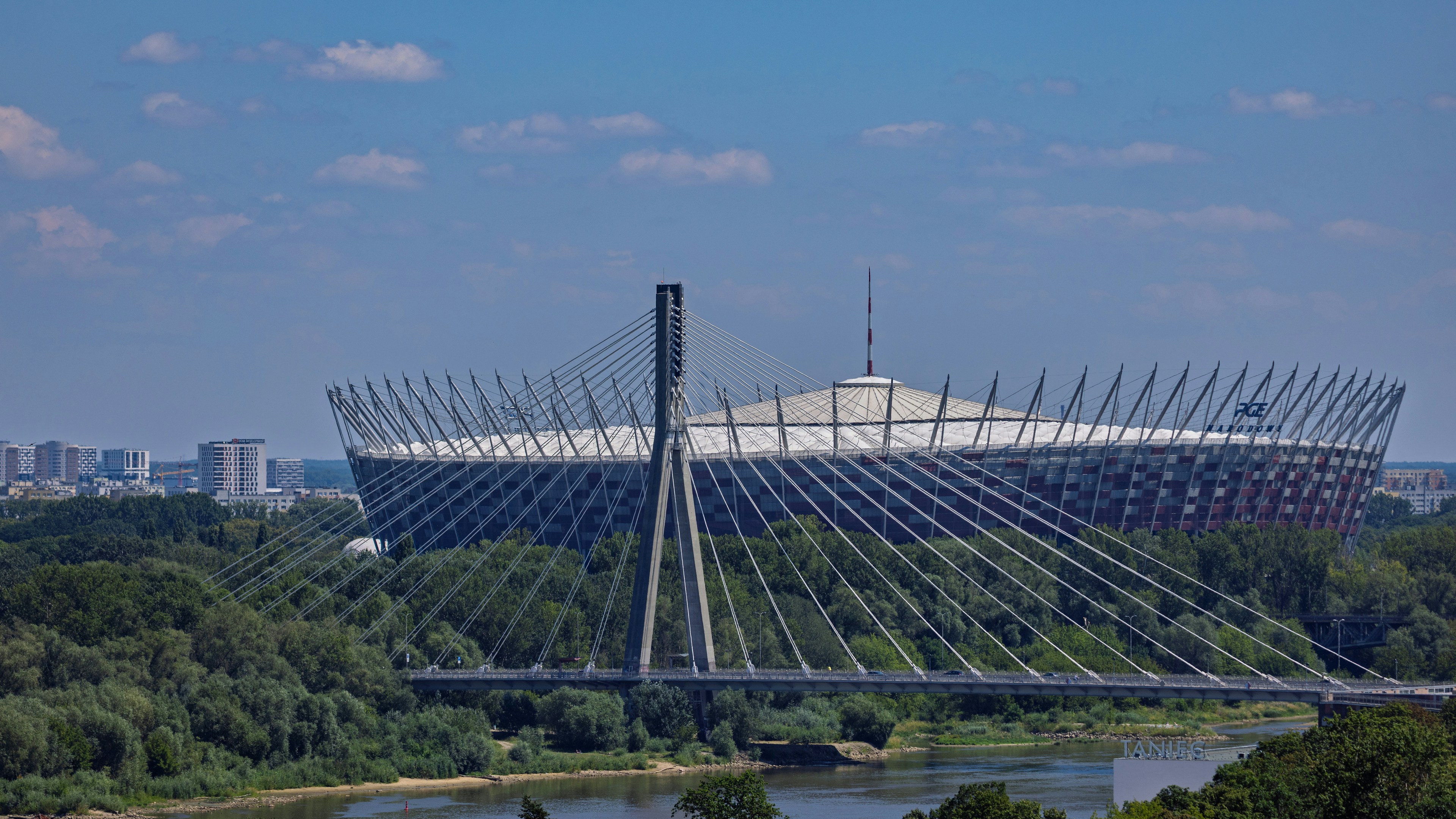 A modern stadium, cable-stayed bridge, and river with lush trees