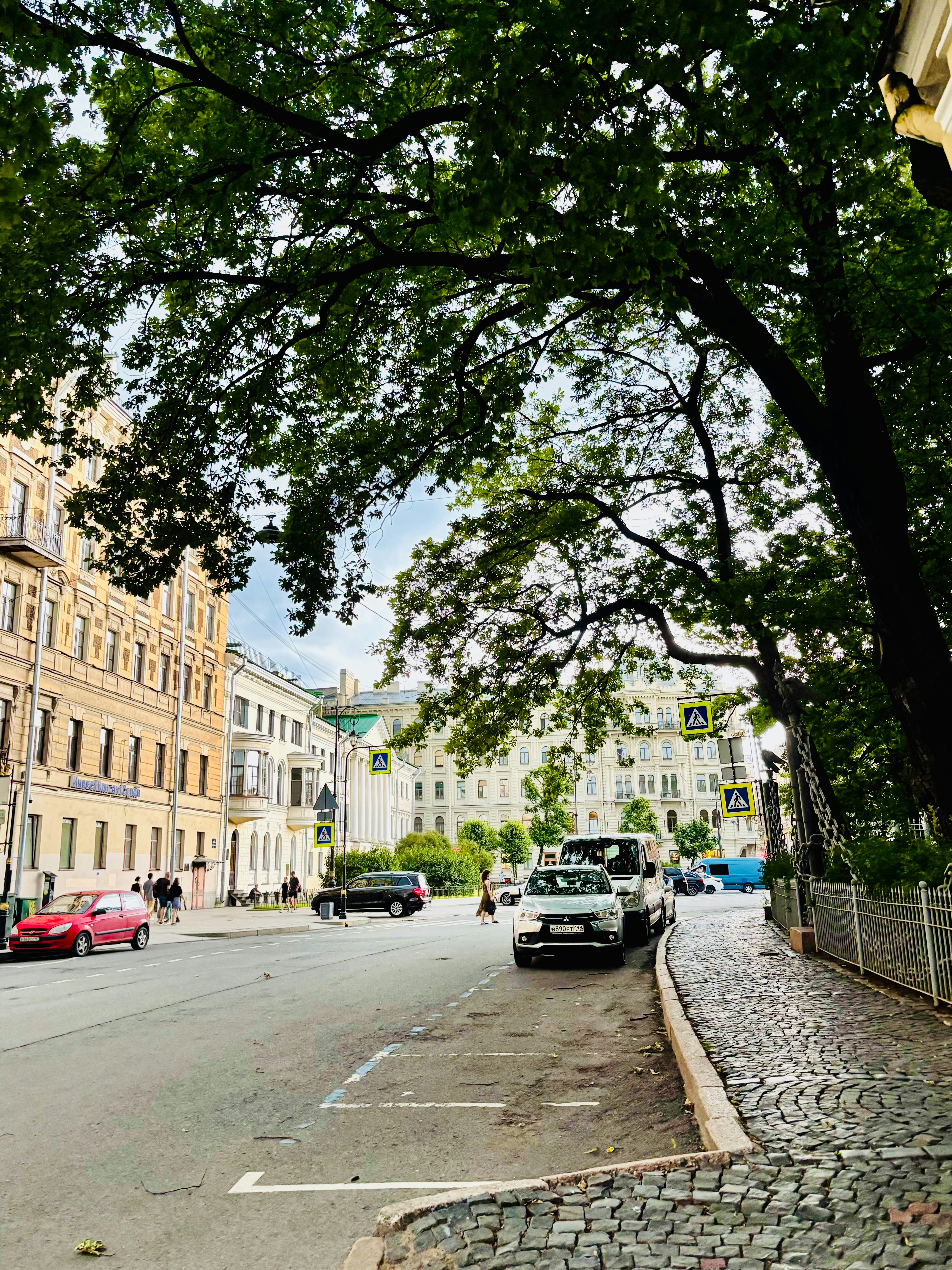Urban street lined with historic buildings and lush green trees.