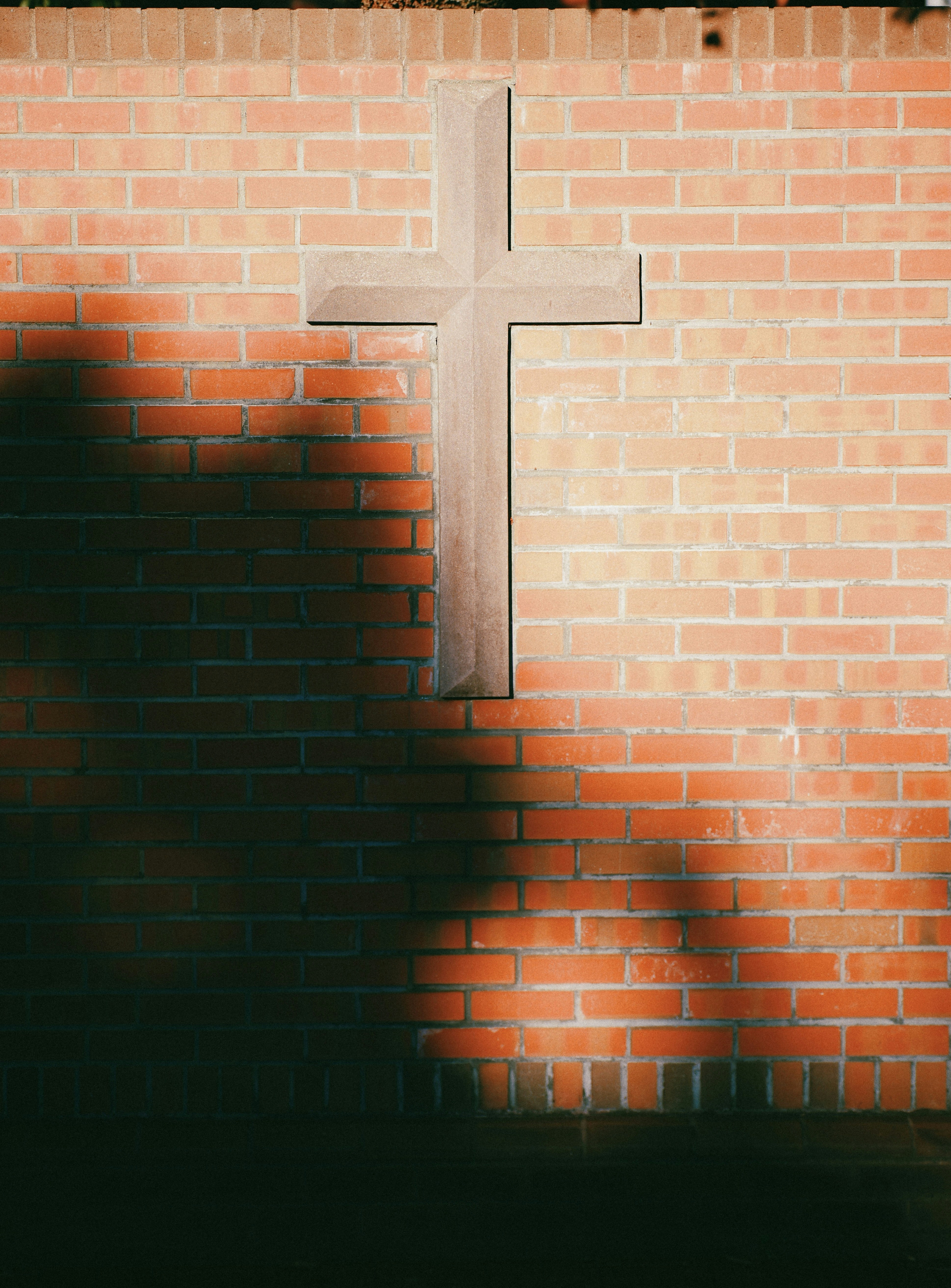 Stone cross on red brick wall with dappled shadows - 相关推荐