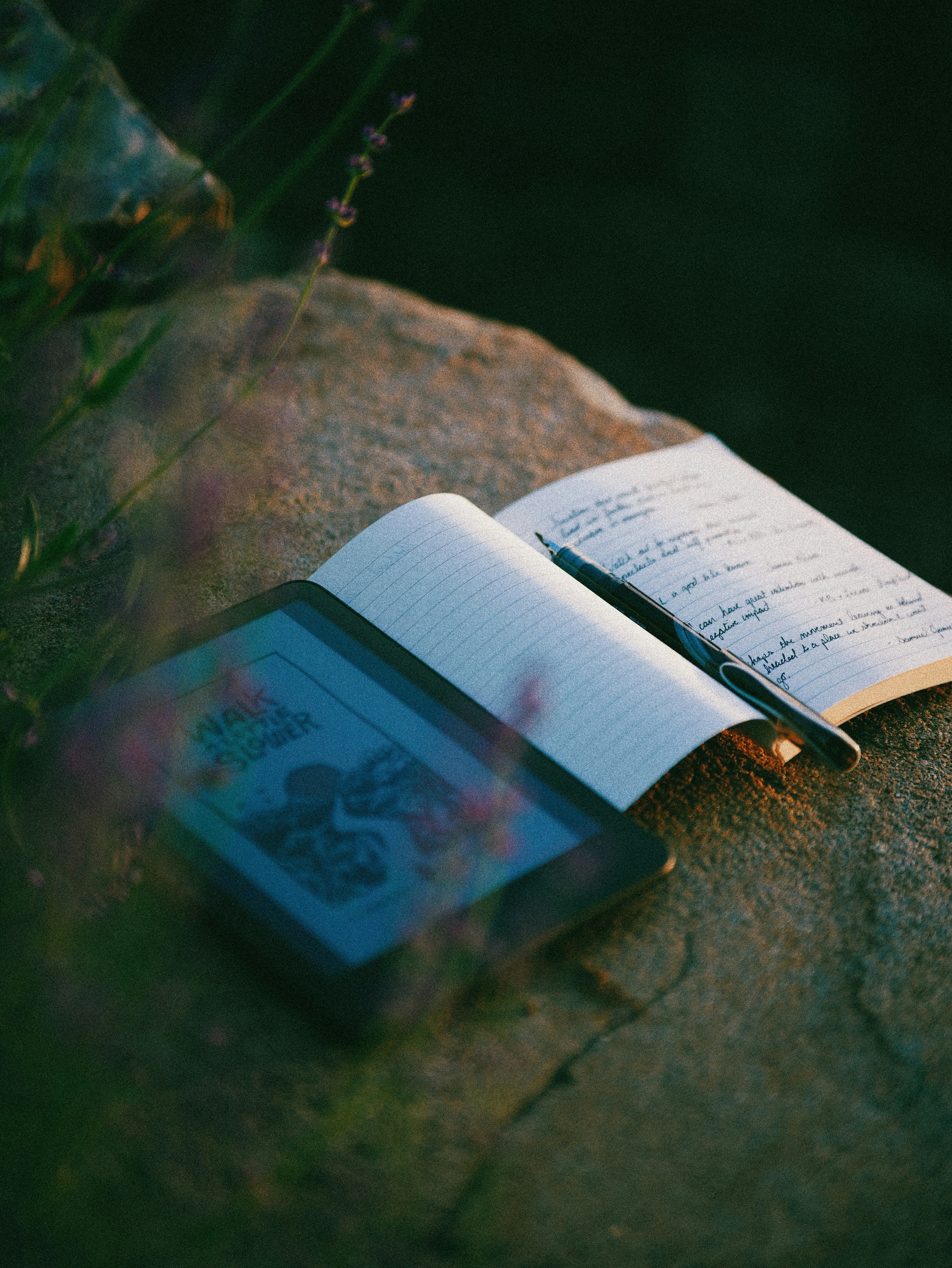 E-reader, open notebook, and pen on a rock