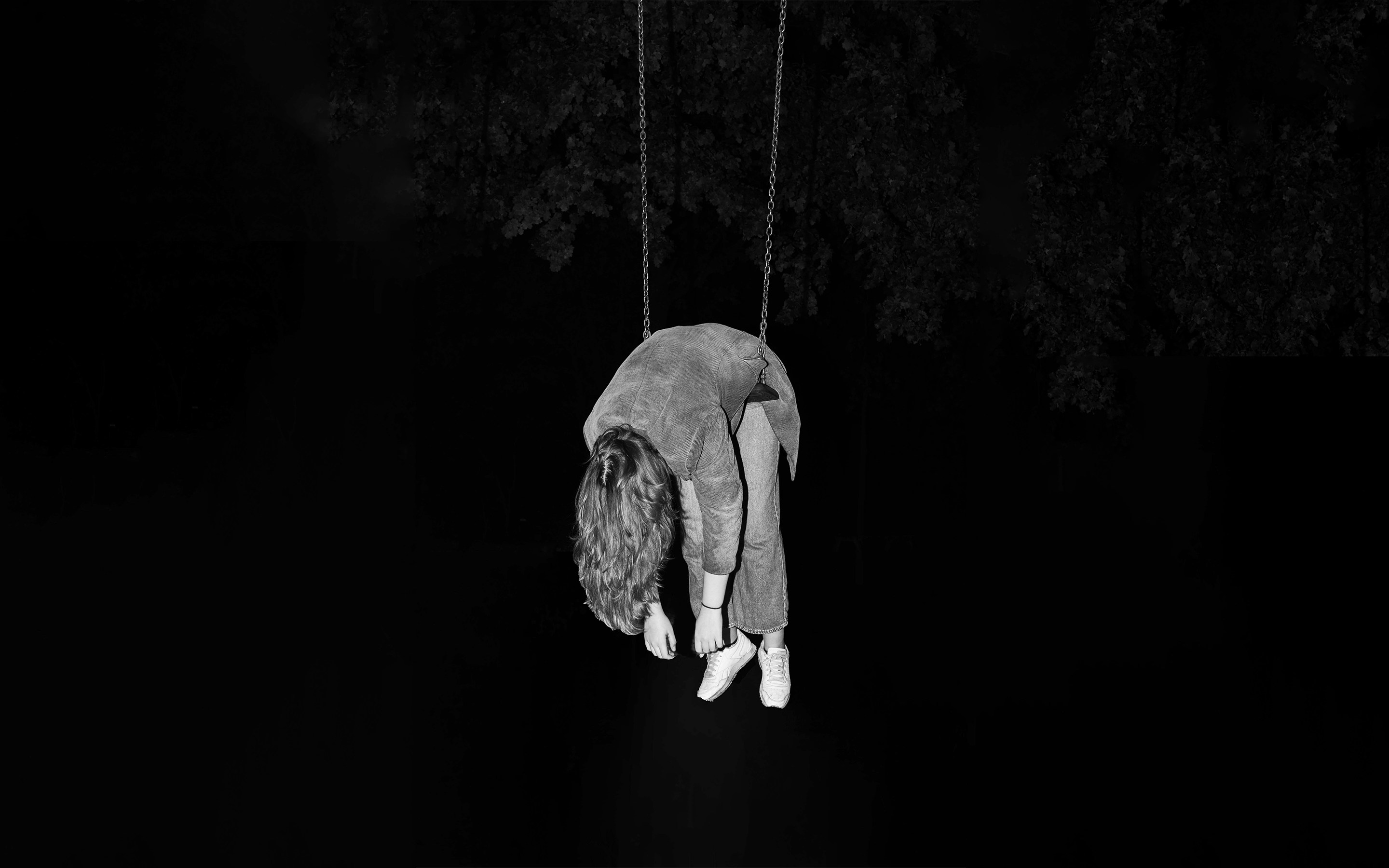 A person hanging upside down from ropes in darkness