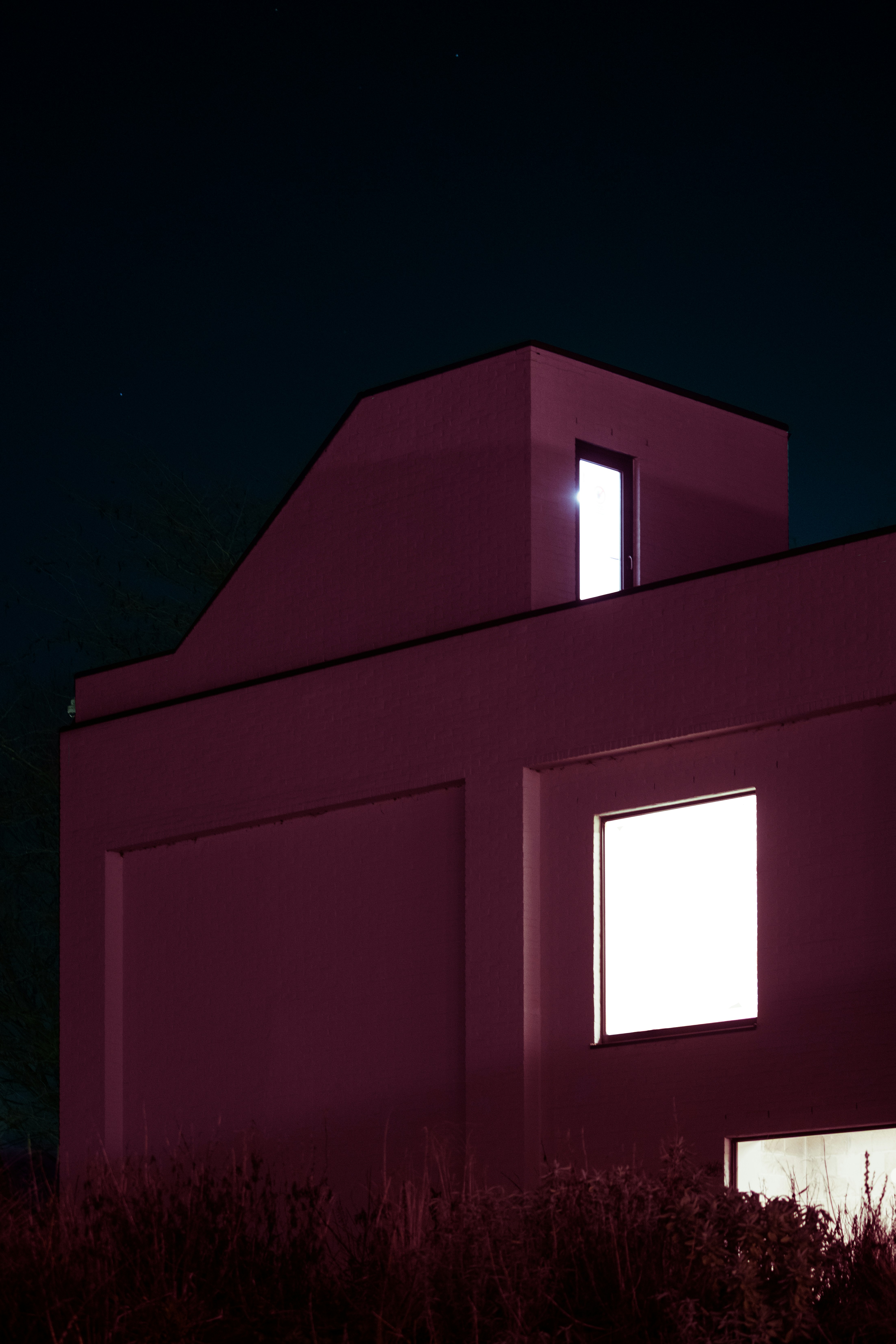 Modernes rosa Gebäude mit hellen Fenstern vor dunkler Nacht.