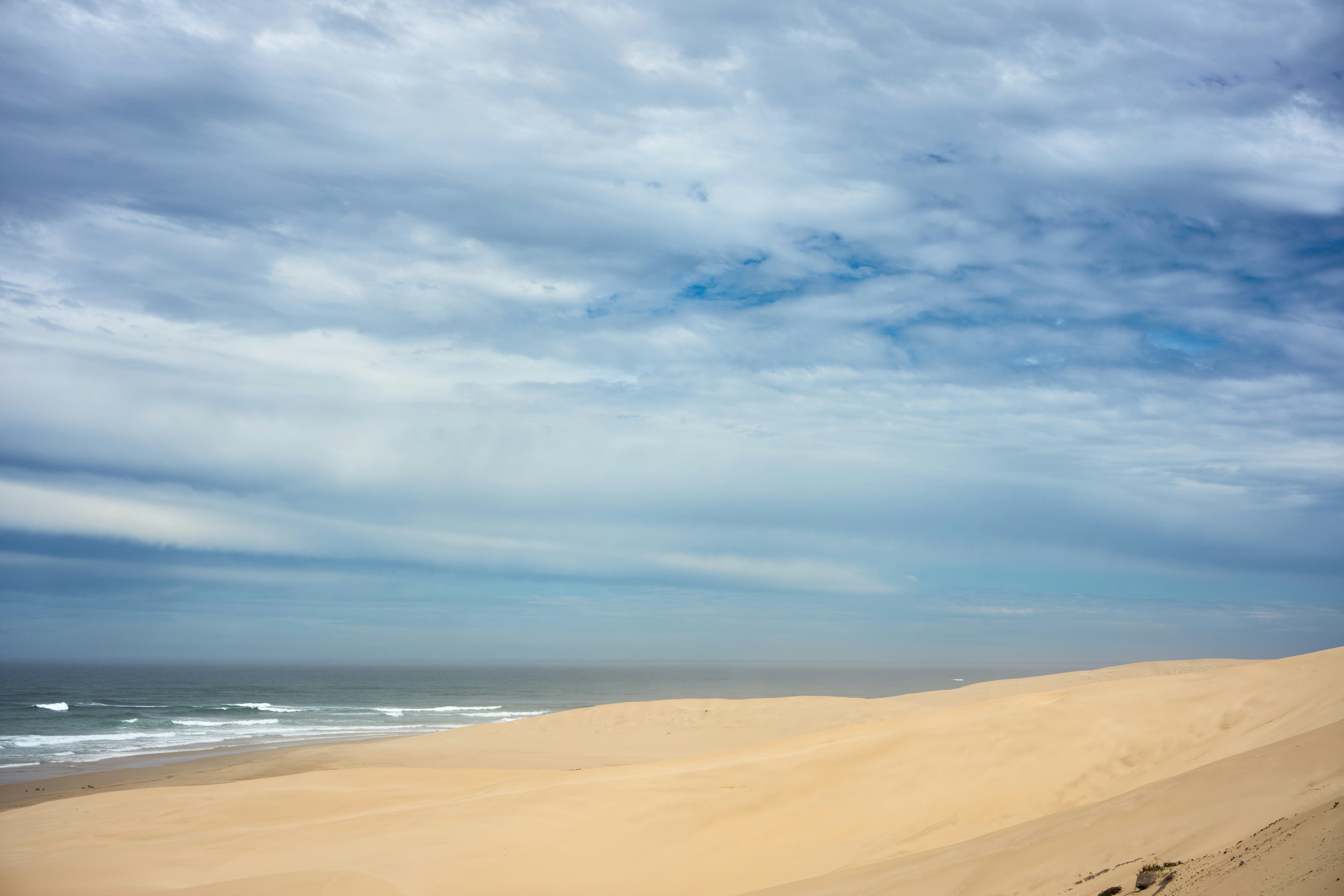 Sandy beach and ocean under a cloudy blue sky.