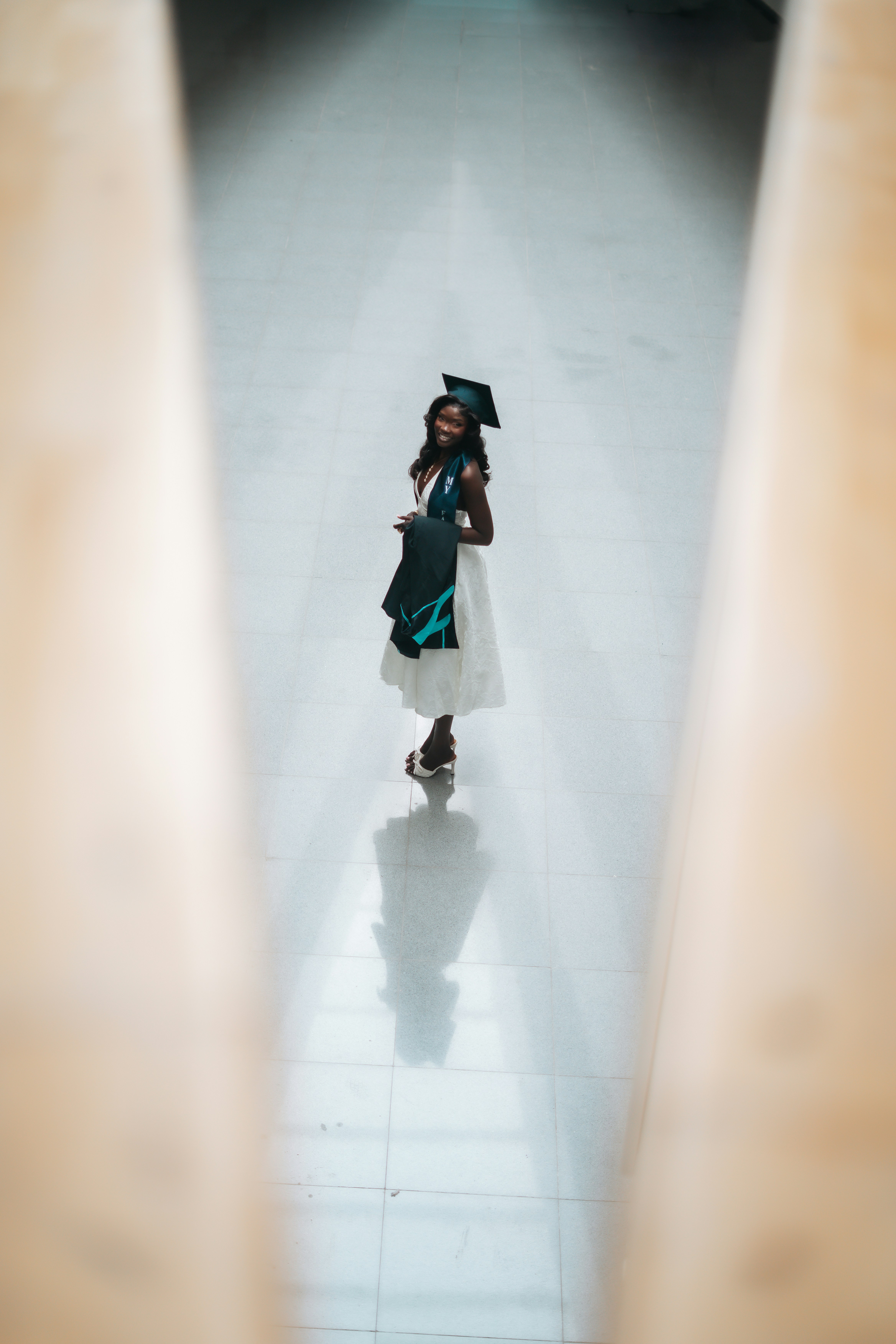 Une femme souriante en tenue de remise des diplômes se tient dans un couloir