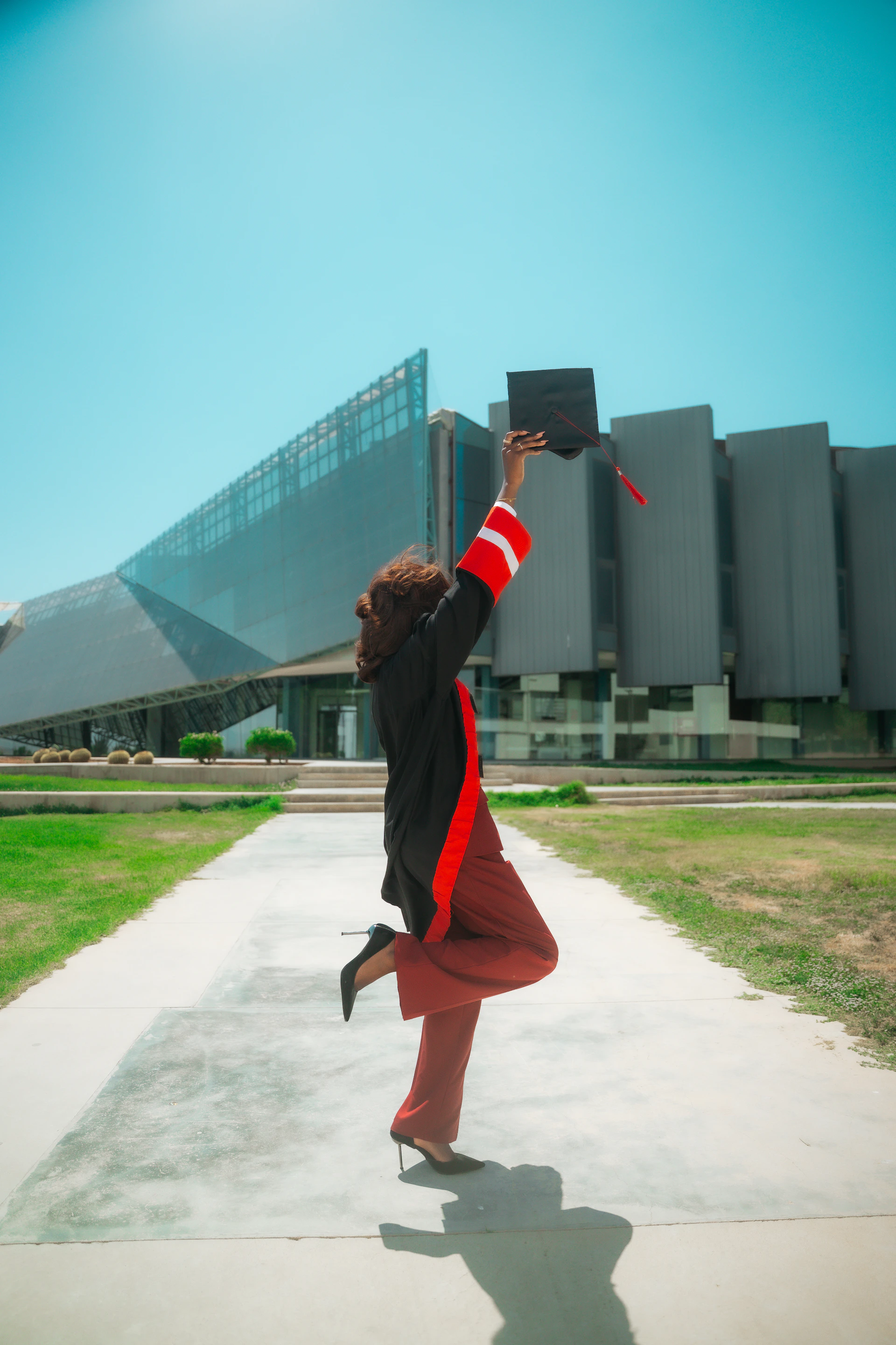 Excited graduate throws cap in air on sunny campus.