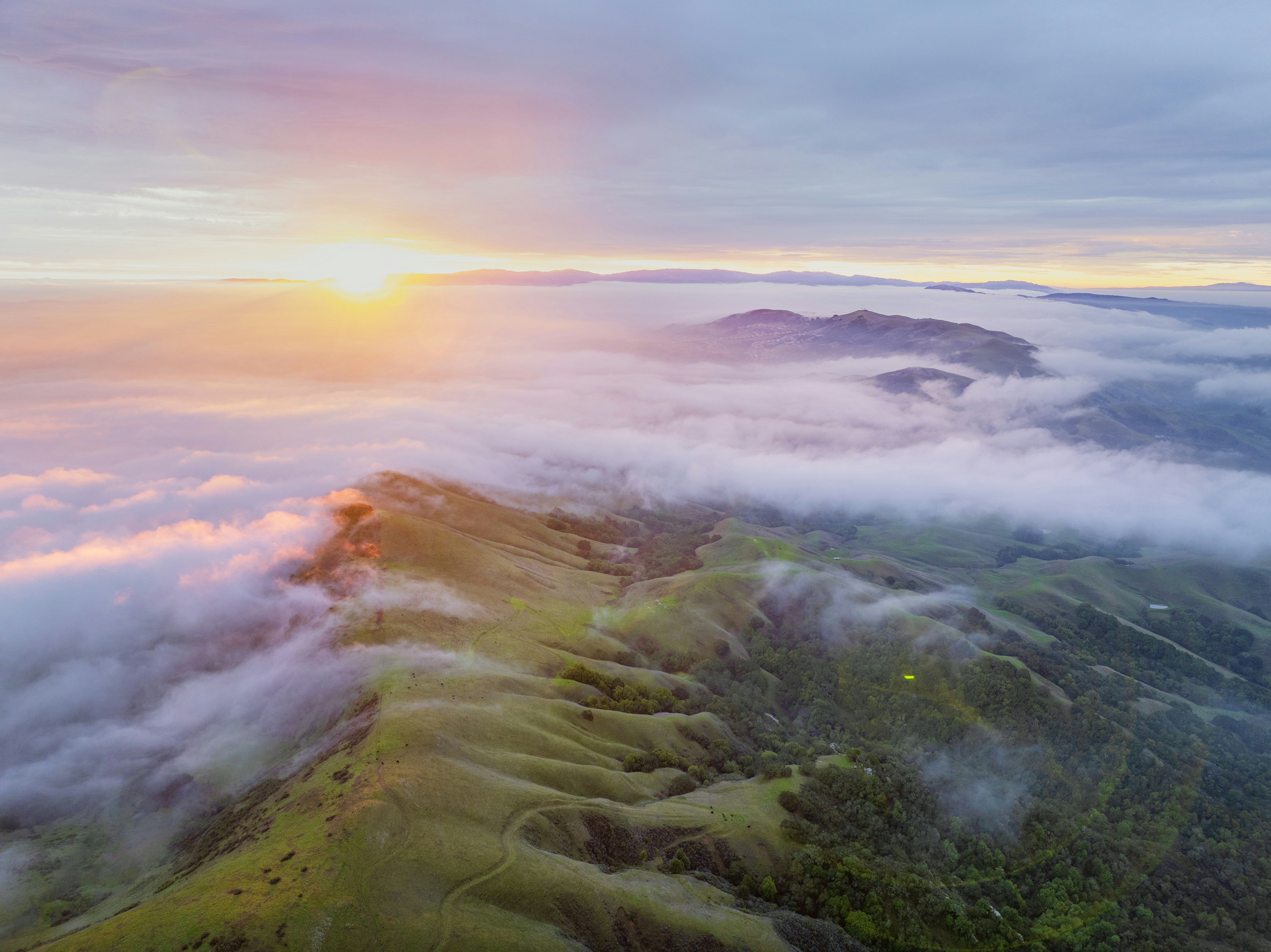 Golden sunrise above rolling green hills and clouds
