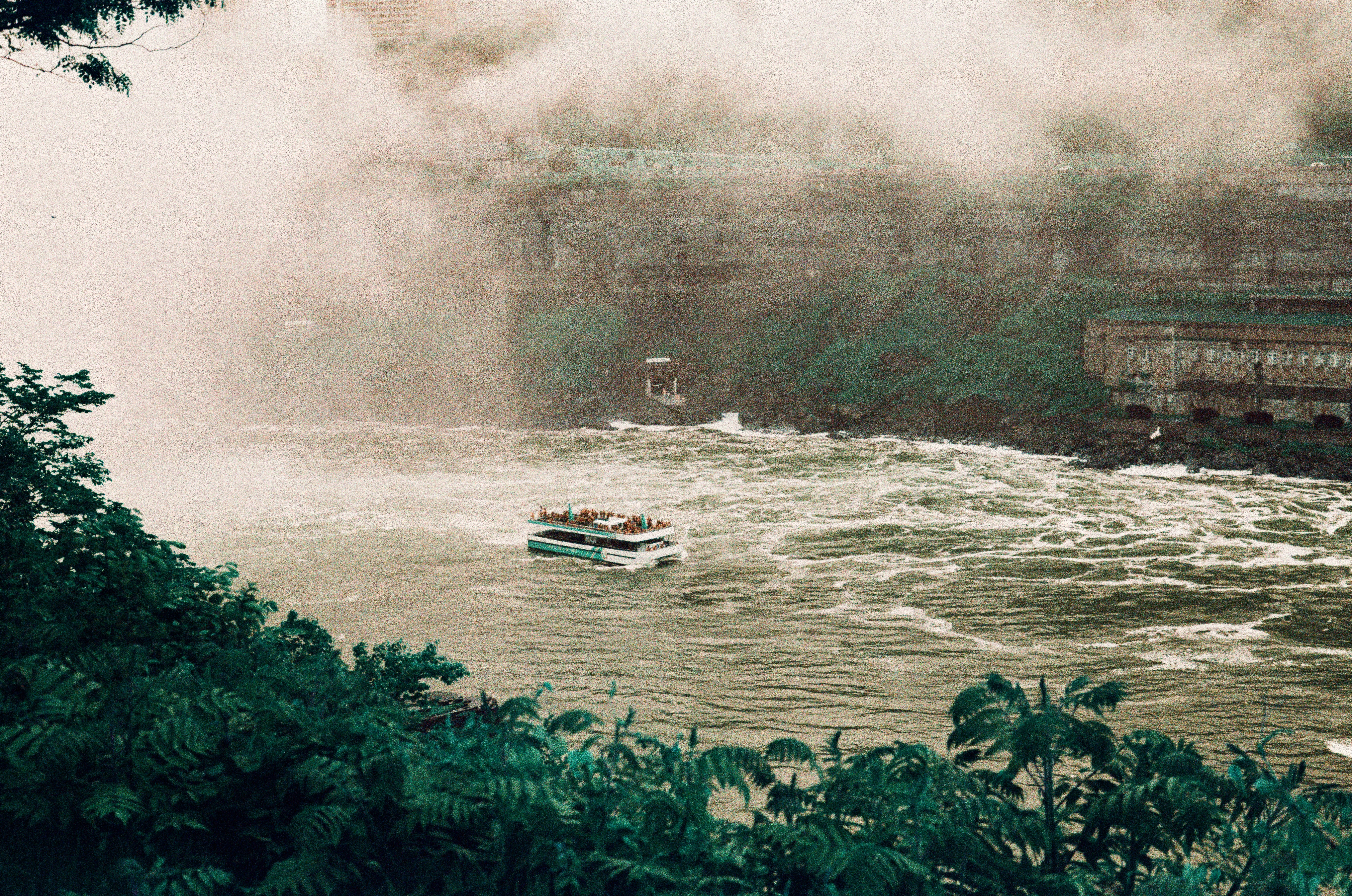 A boat navigates turbulent waters near a powerful waterfall