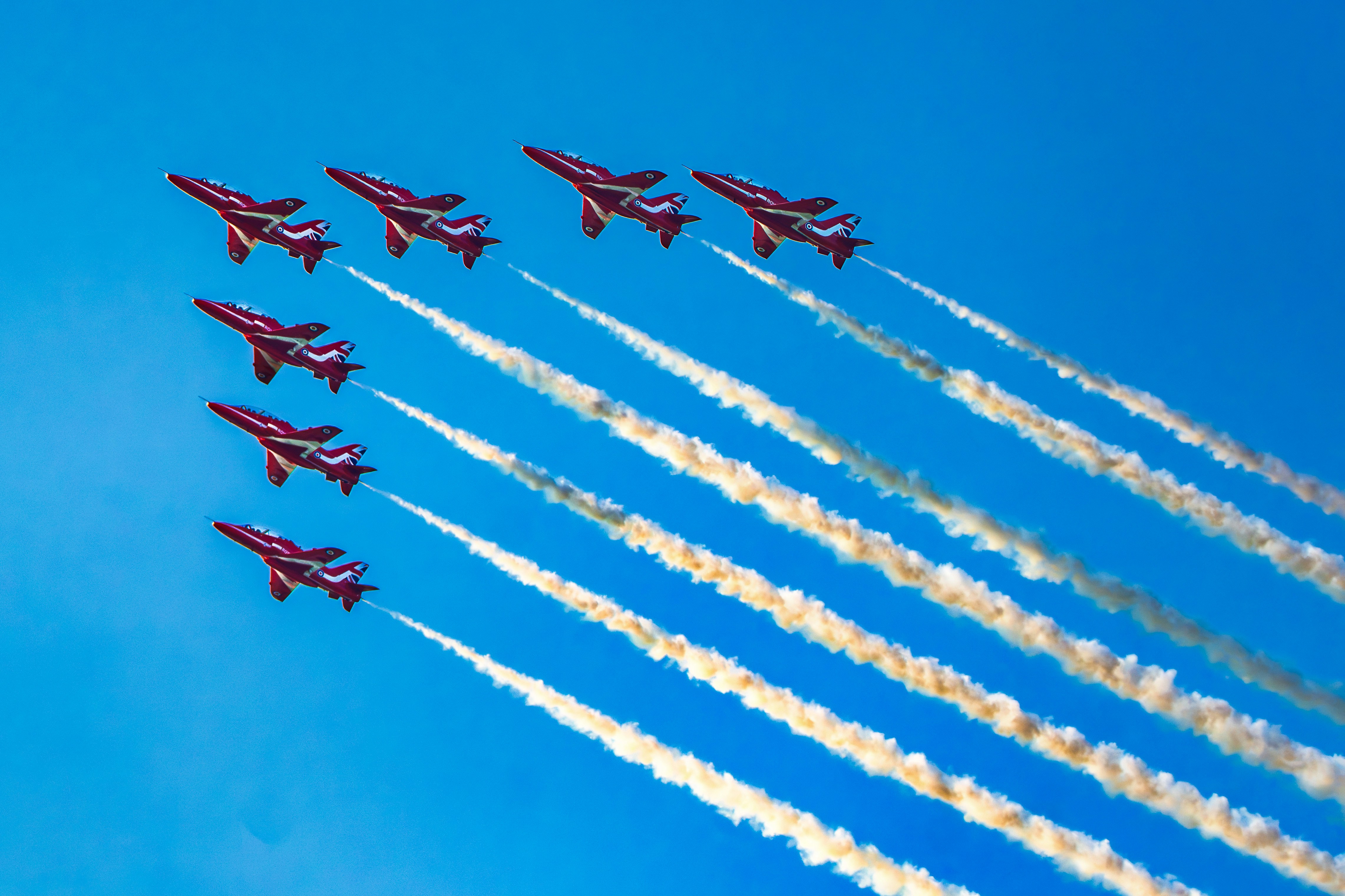 Sept avions rouges effectuent des démonstrations aériennes avec des traînées de fumée blanche.