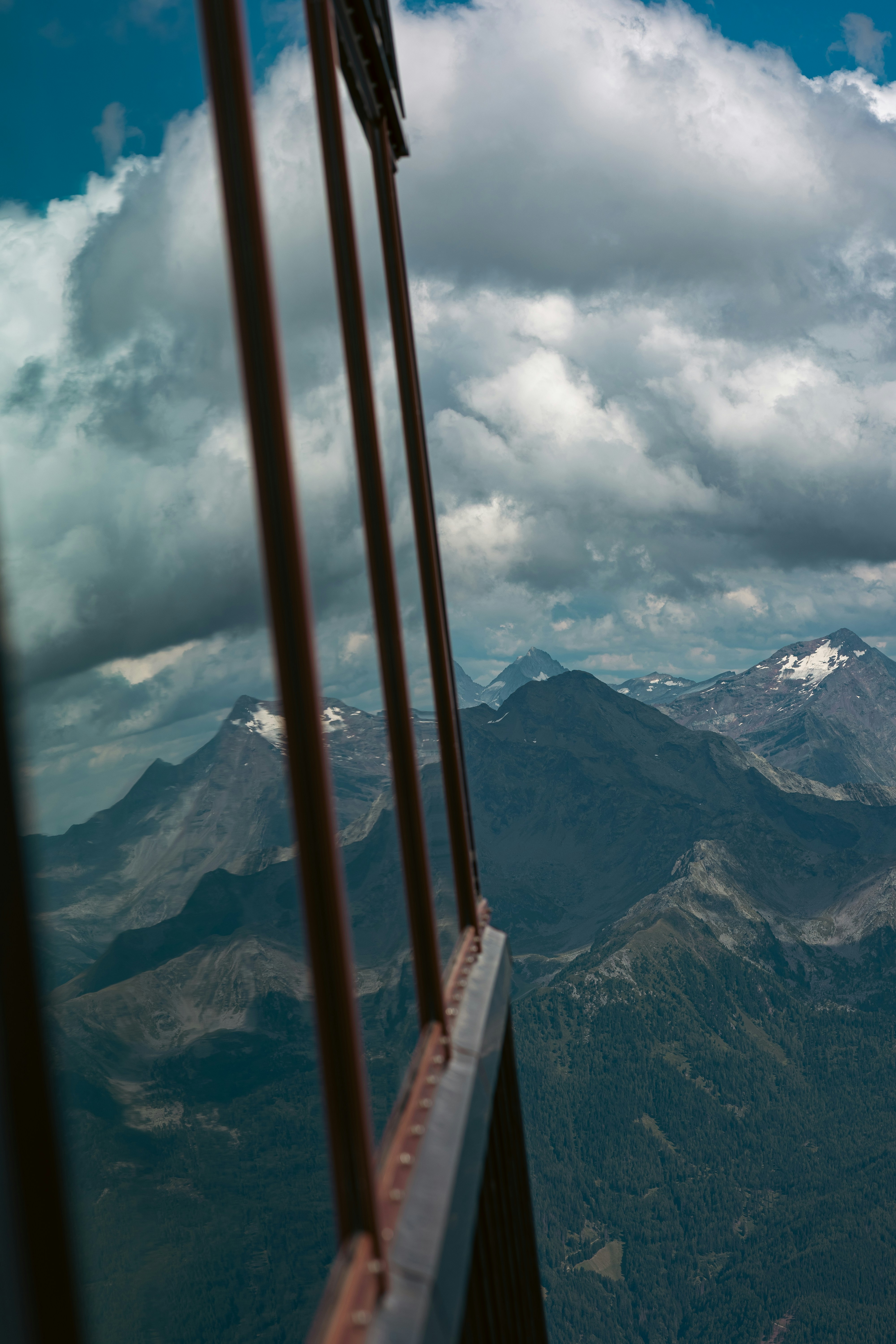 Snow-capped mountains and cloudy sky framed by a railing.