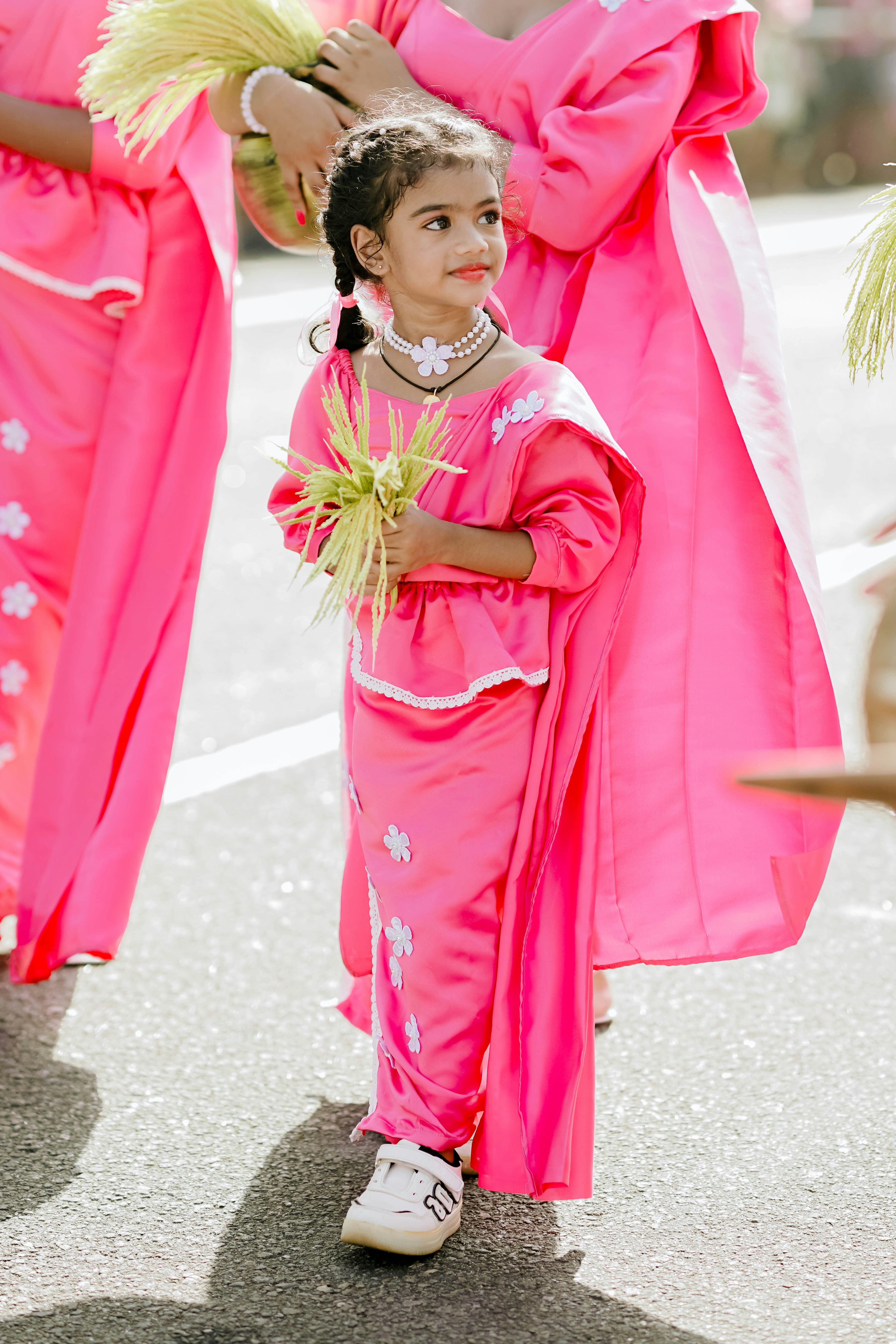 Young girl in pink traditional dress holds green stalks.