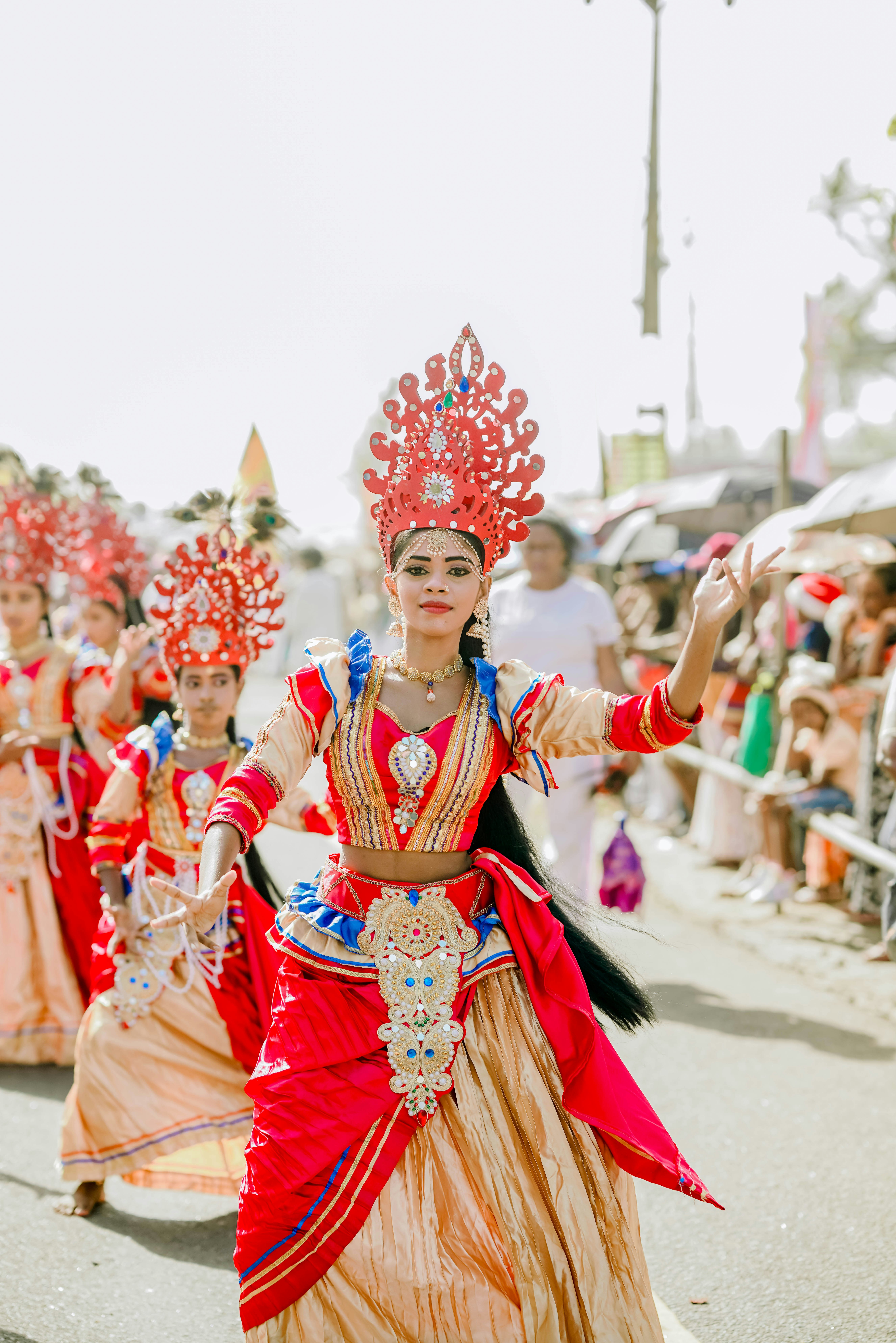 Traditional dancer in elaborate red and gold costume performs outdoors.