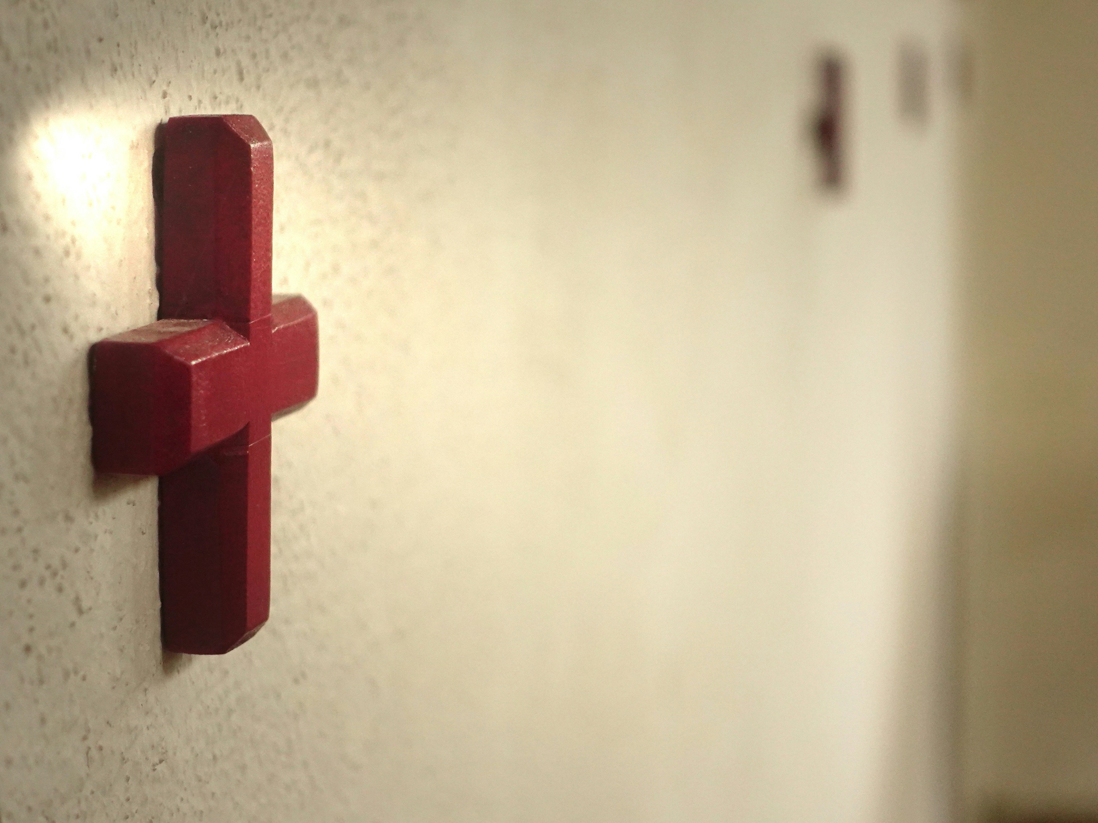 Illuminated red wooden cross on a wall with others receding.