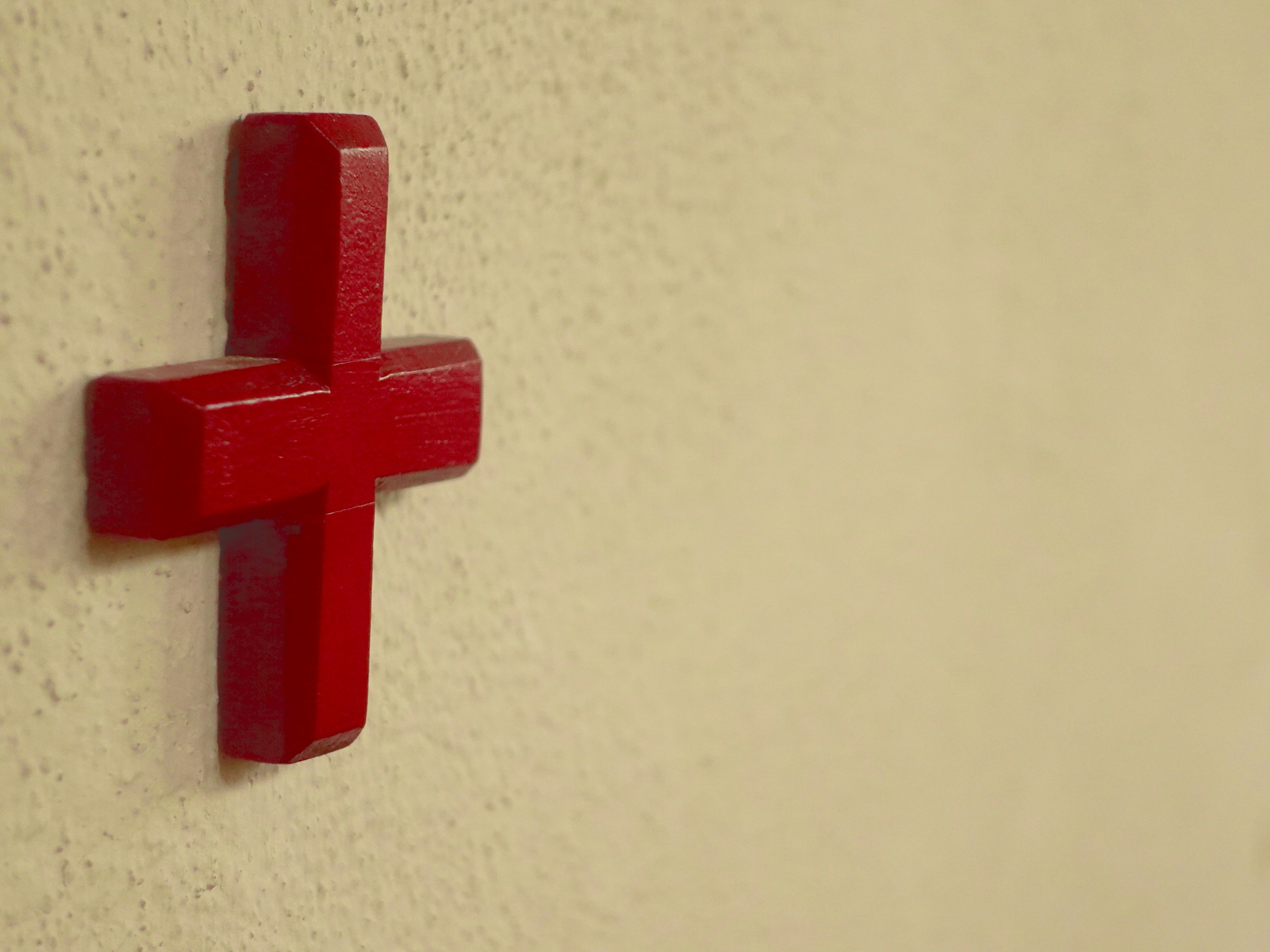 Ein rotes Plus-Schild an einer strukturierten gelben Wand.