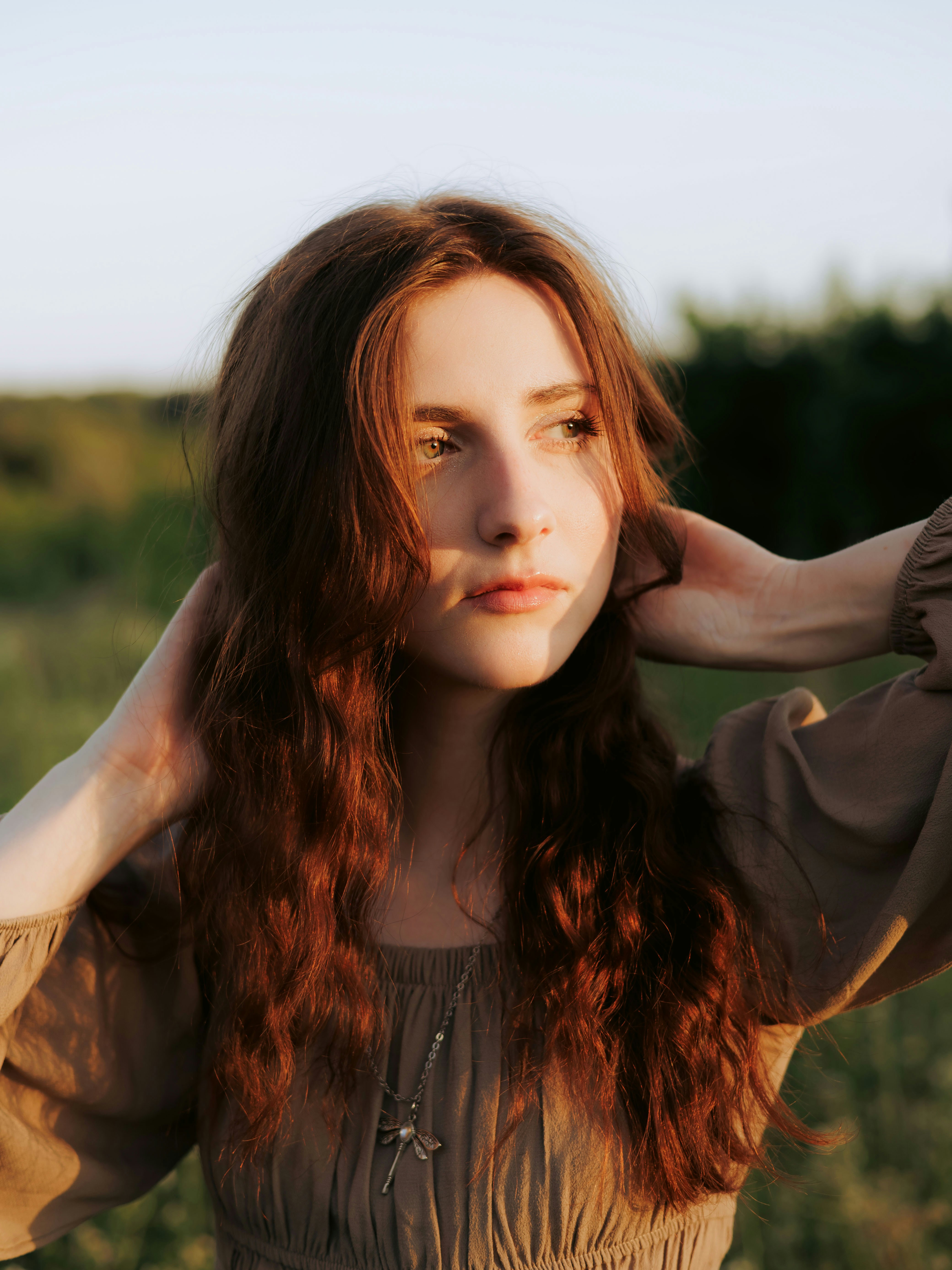 Junge Frau mit roten Haaren auf einem sonnenbeschienenen Feld.