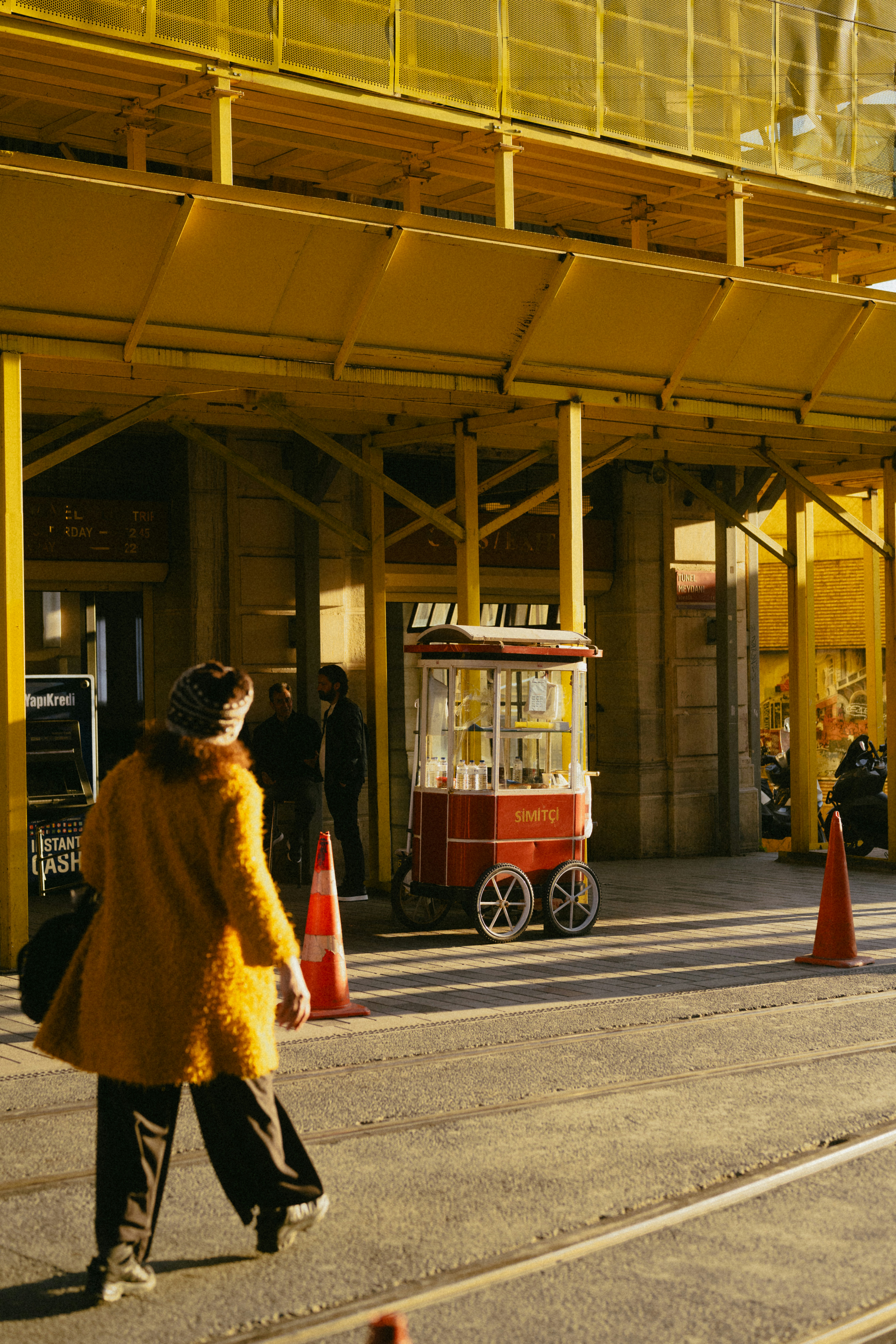 Person walks past a red vendor cart and yellow scaffolding.