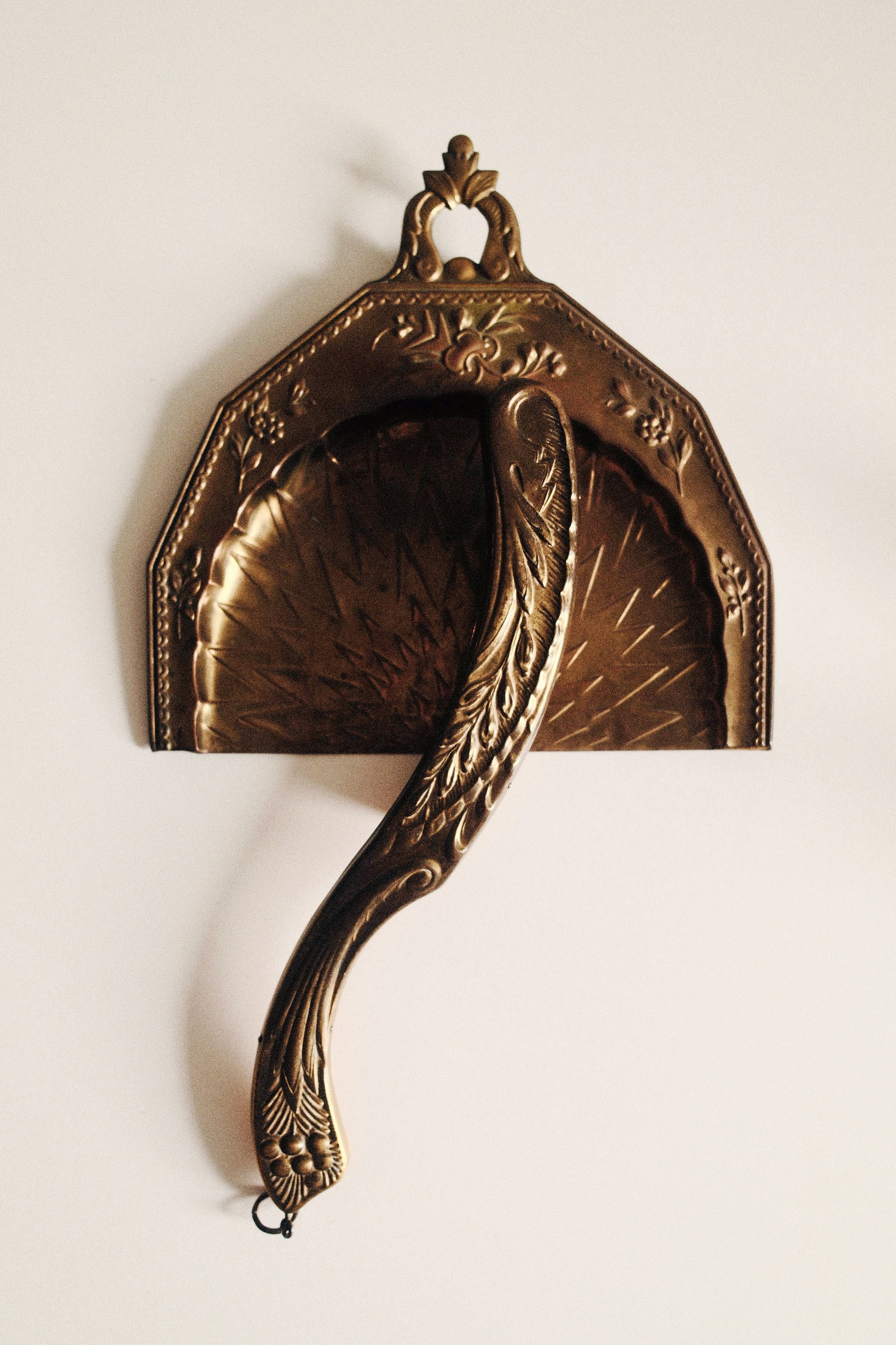 Ornate brass dustpan and brush hanging on white wall