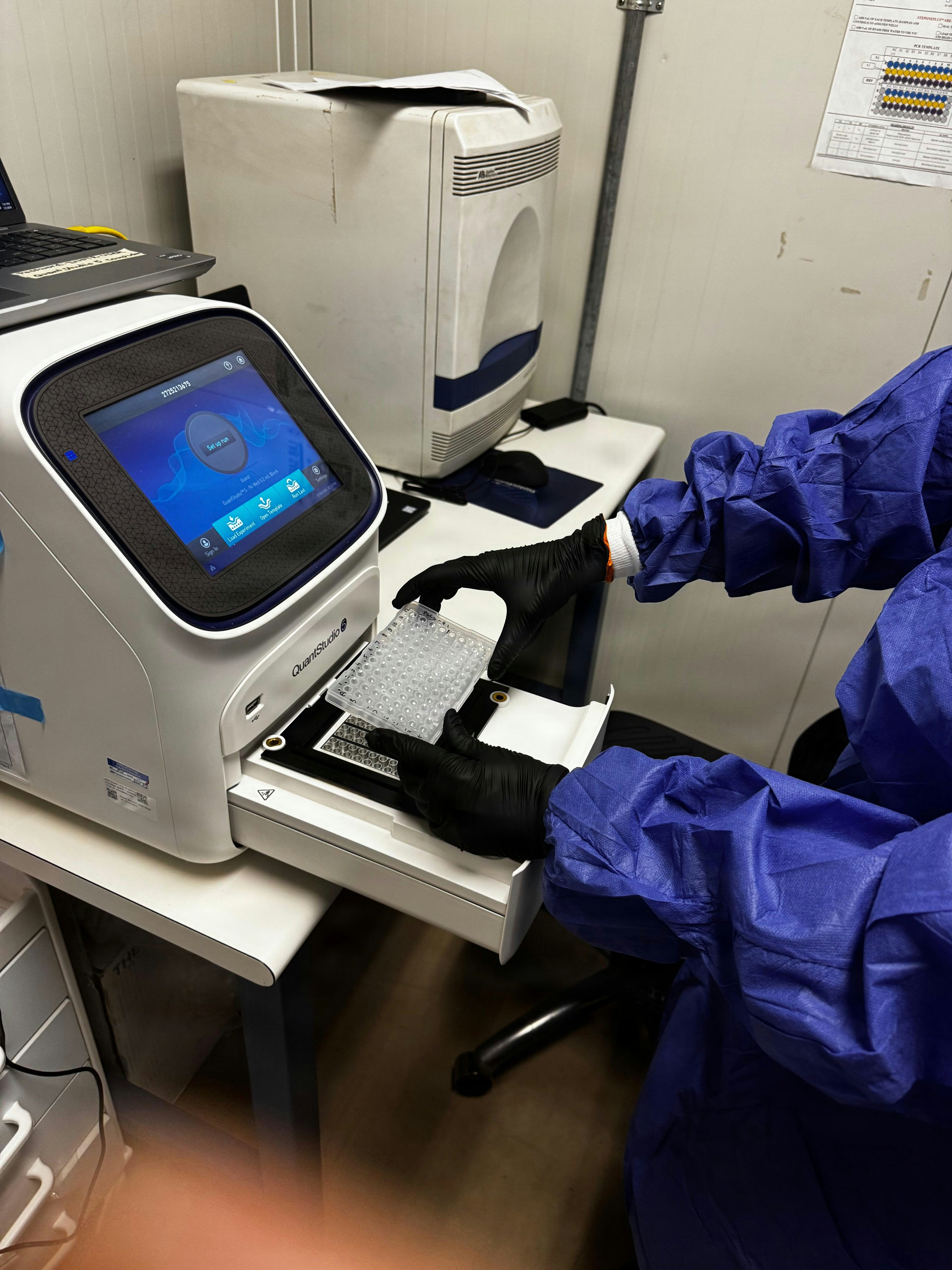 Person in ppe loads sample into laboratory testing machine.
