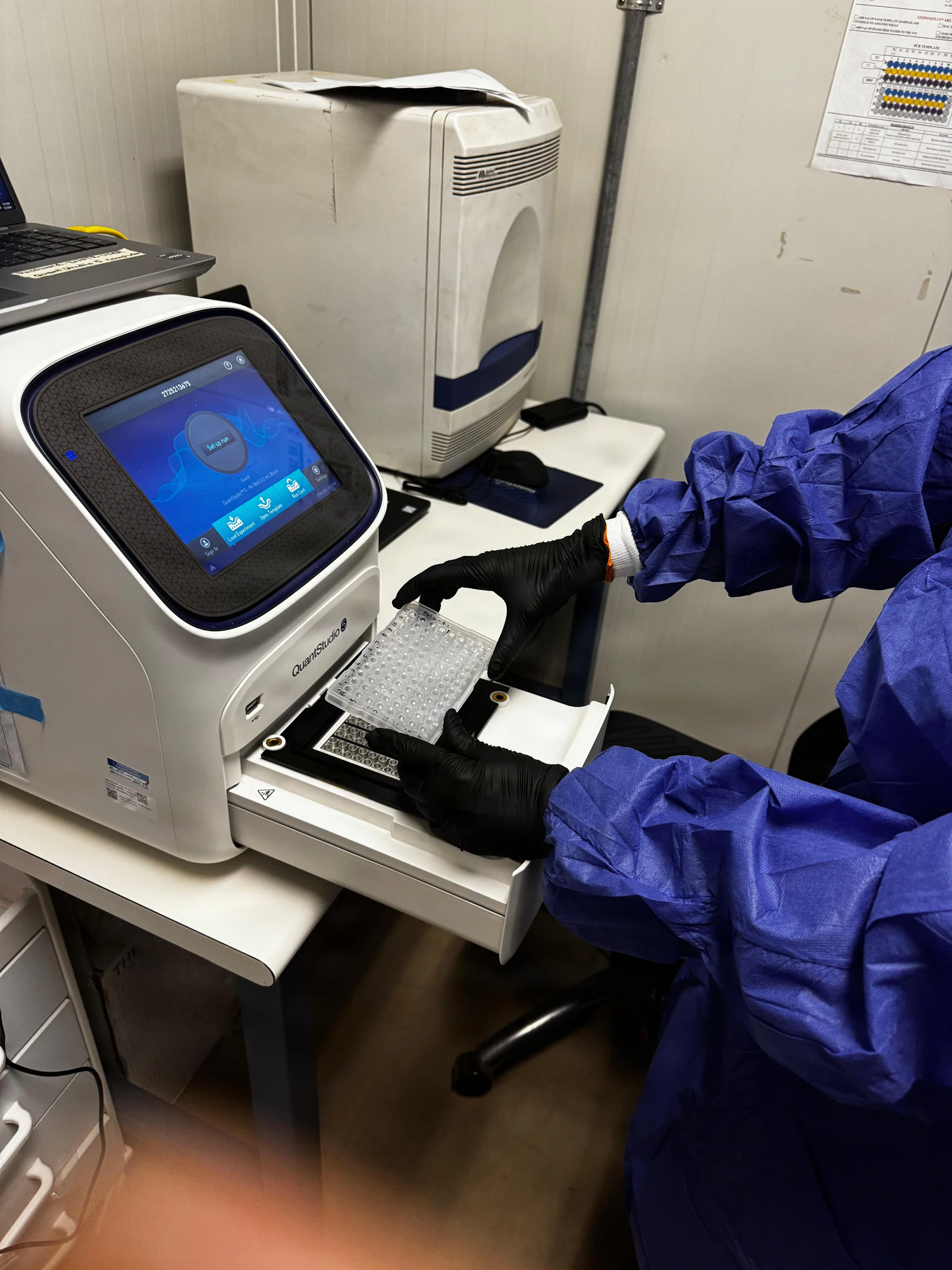 Technologist in PPE loading a sample into a laboratory testing machine