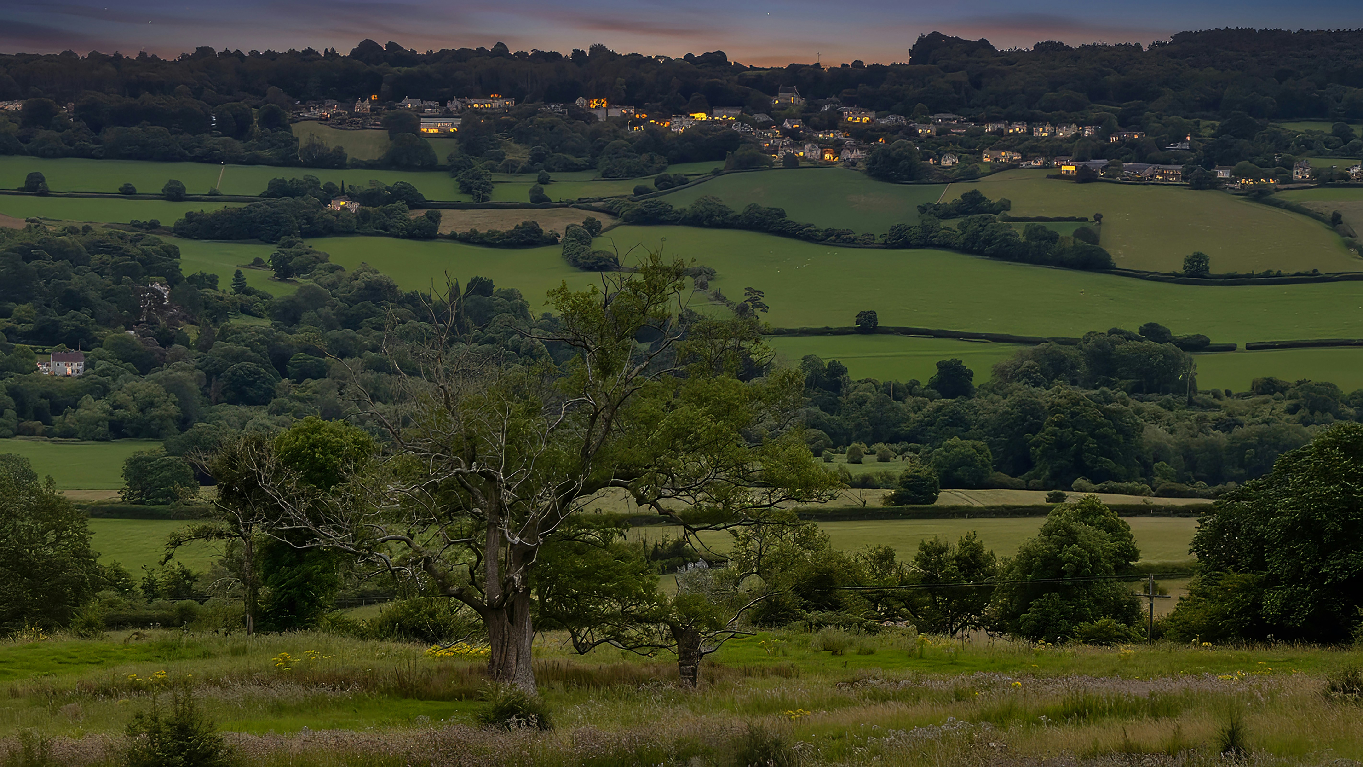 Rural landscape with green hills and distant village at dusk.