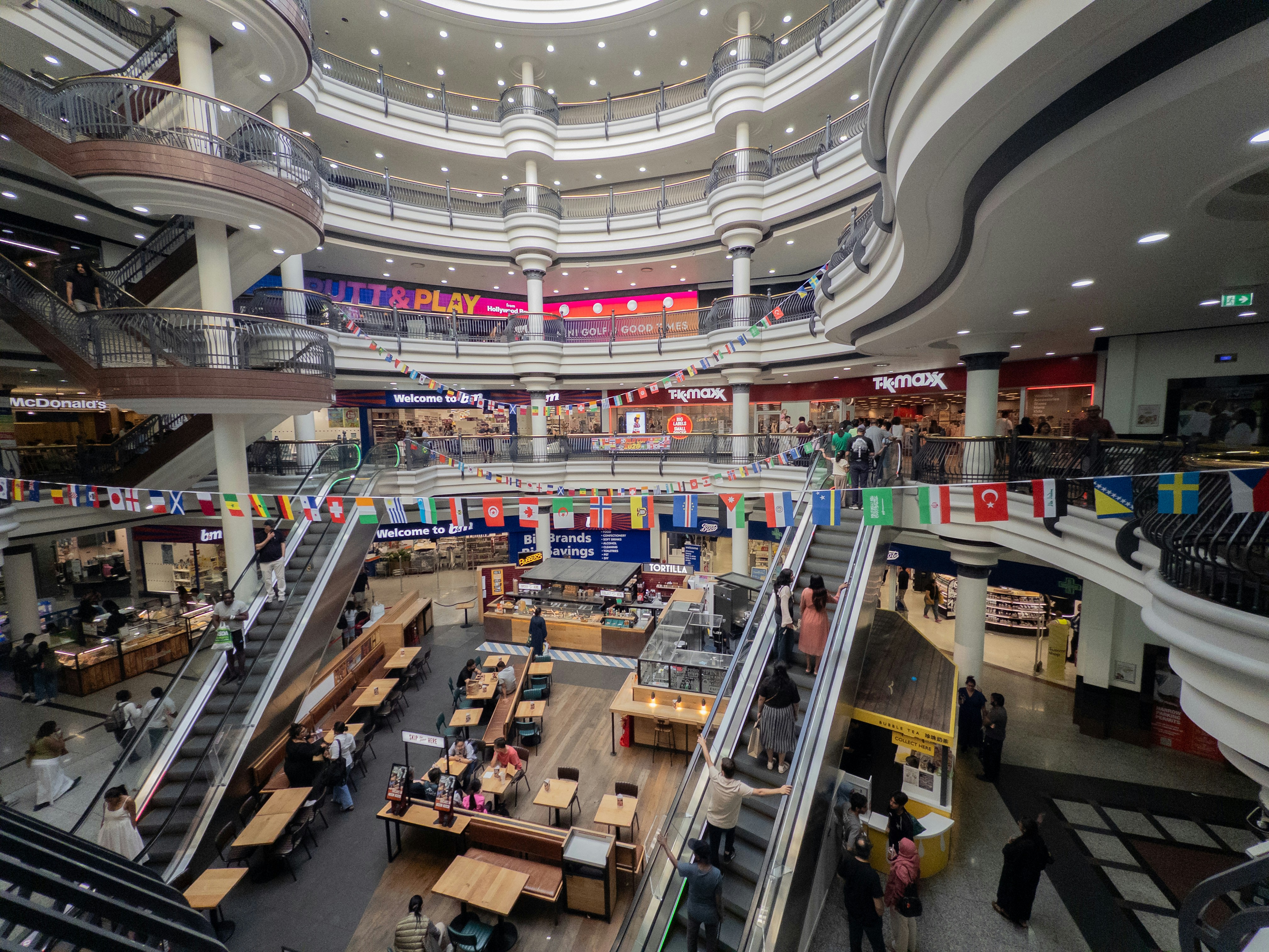 A bustling multi-story shopping mall interior with escalators and shops.