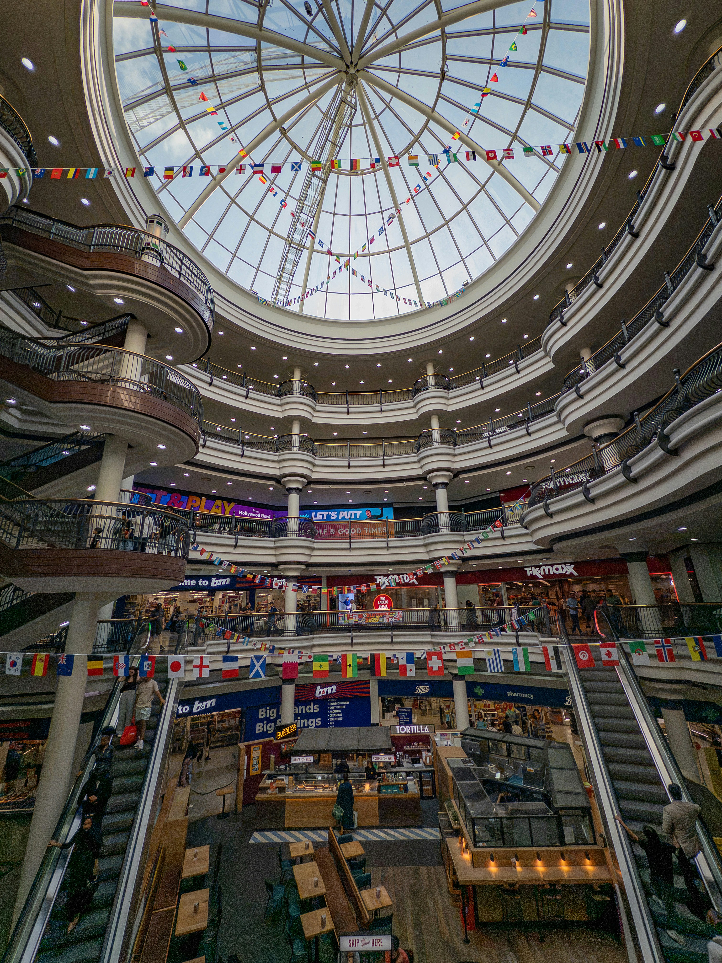 Multi-level shopping mall interior with escalators and glass dome.