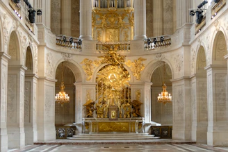 Ornate golden altar inside a grand, historic chapel with chandeliers