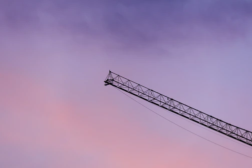 A crane boom against a vibrant purple and pink sky