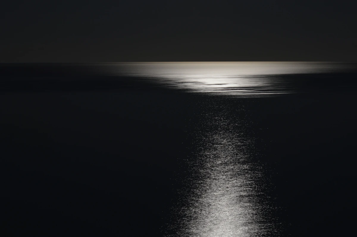 Traînée de lumière lunaire réfléchie sur une mer sombre et calme, la nuit