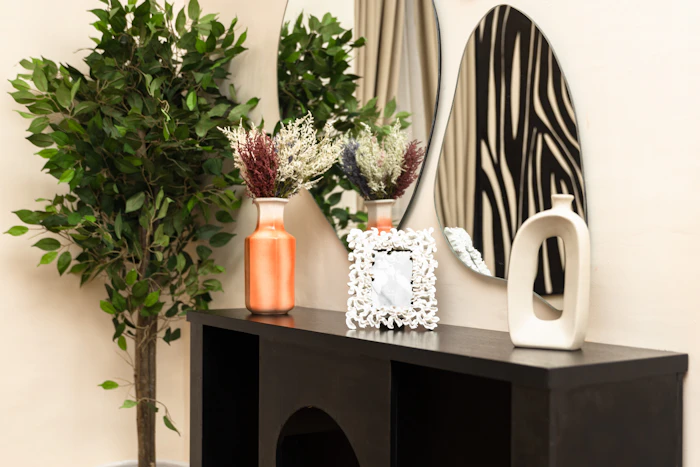 A console styled with a mirror, vases and greenery